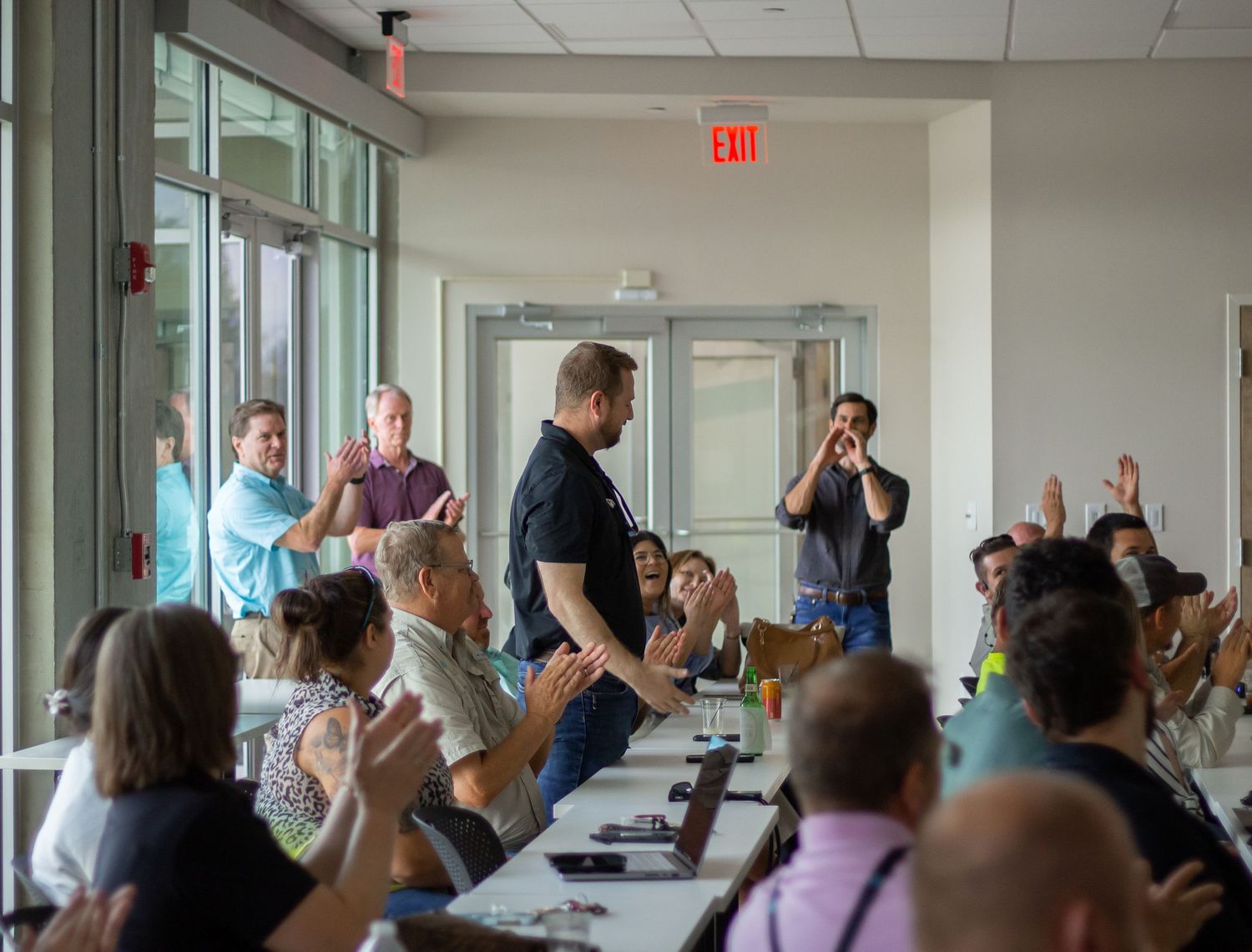 A large group of people in a conference room raise their hands during a meeting or presentation.