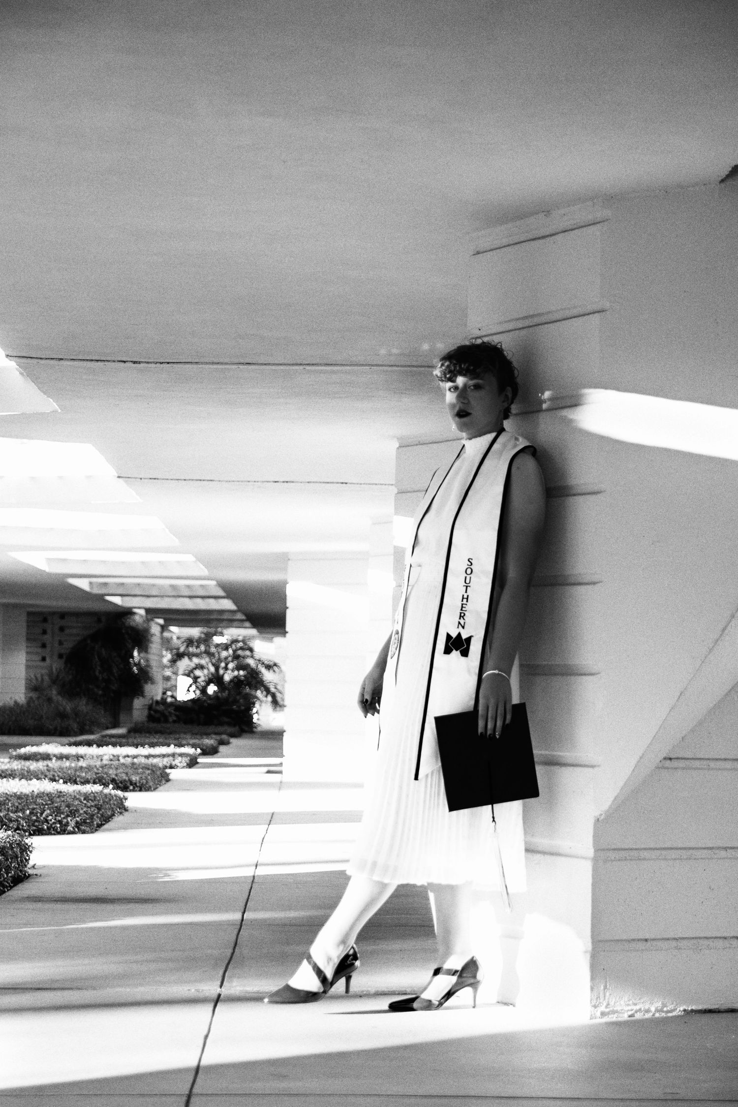 A vintage black and white photo shows a nurse in uniform standing against a white building wall.