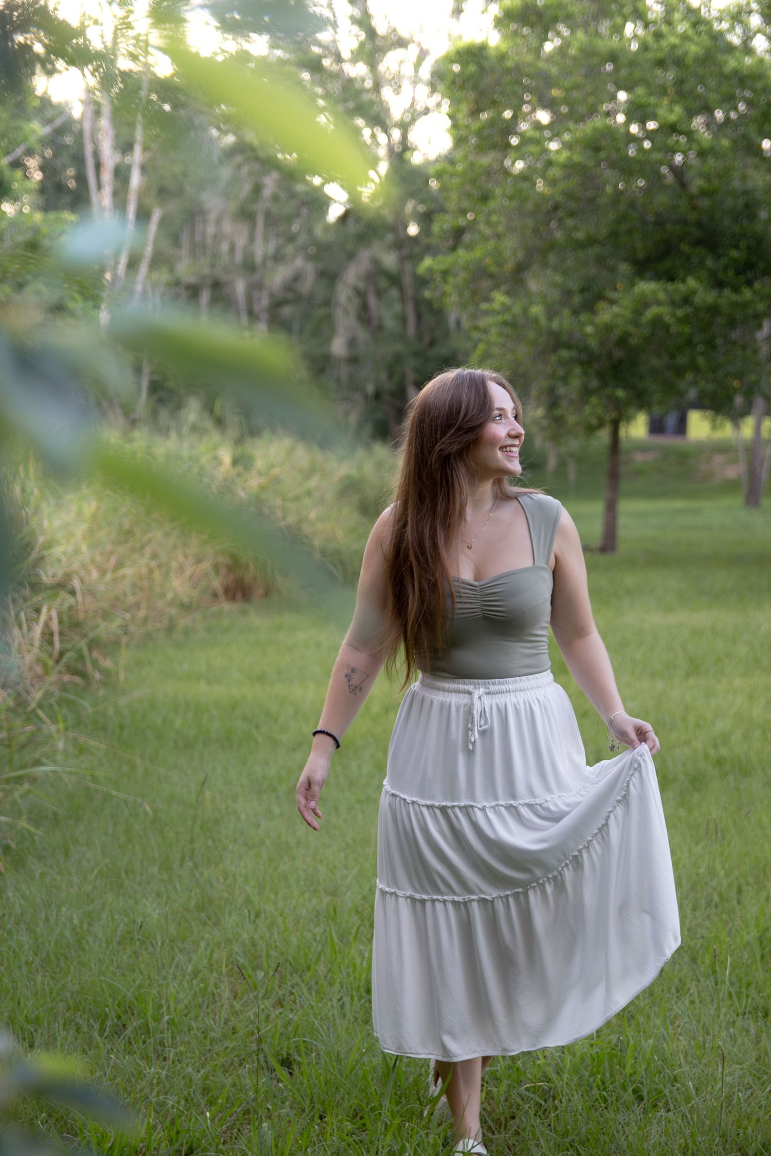 A person in a grey top and white skirt twirls playfully in a sunlit meadow.