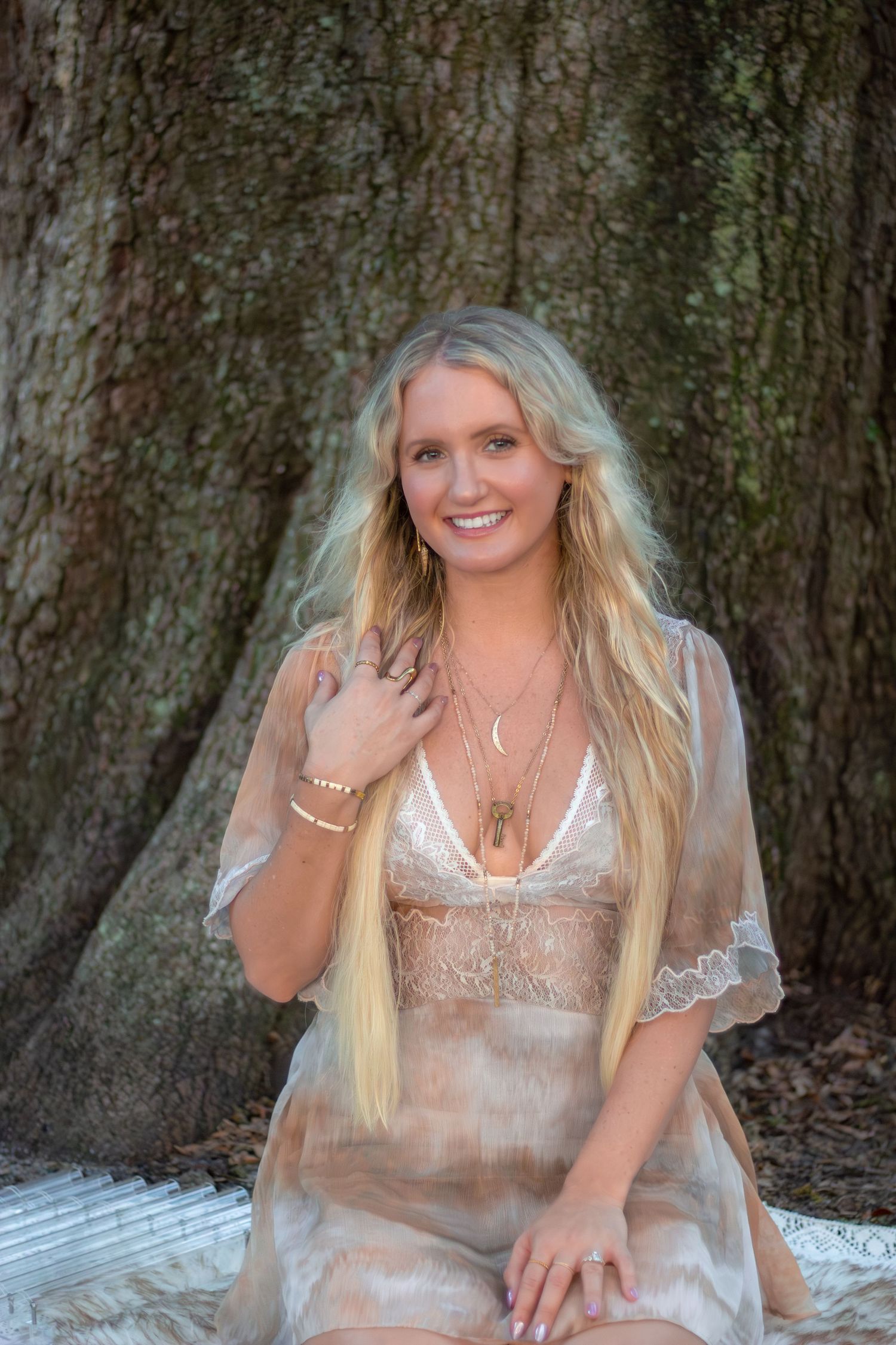 A person in a sparkly cream-colored dress poses against a tree trunk background in a series of outdoor portraits.