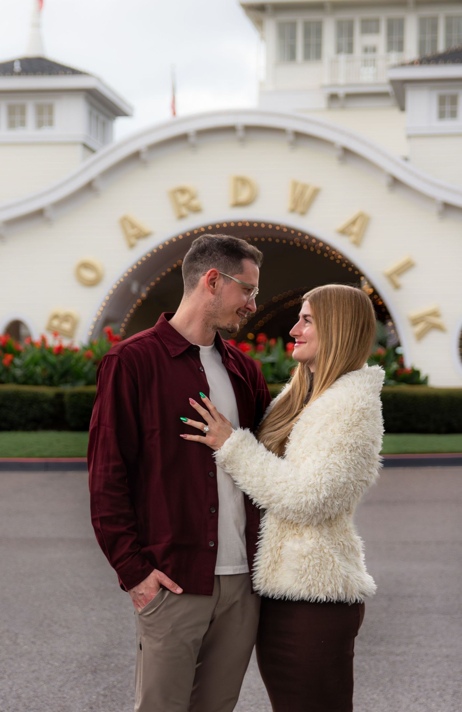 A couple in burgundy and cream outfits share playful moments together outside a building with elegant architecture.