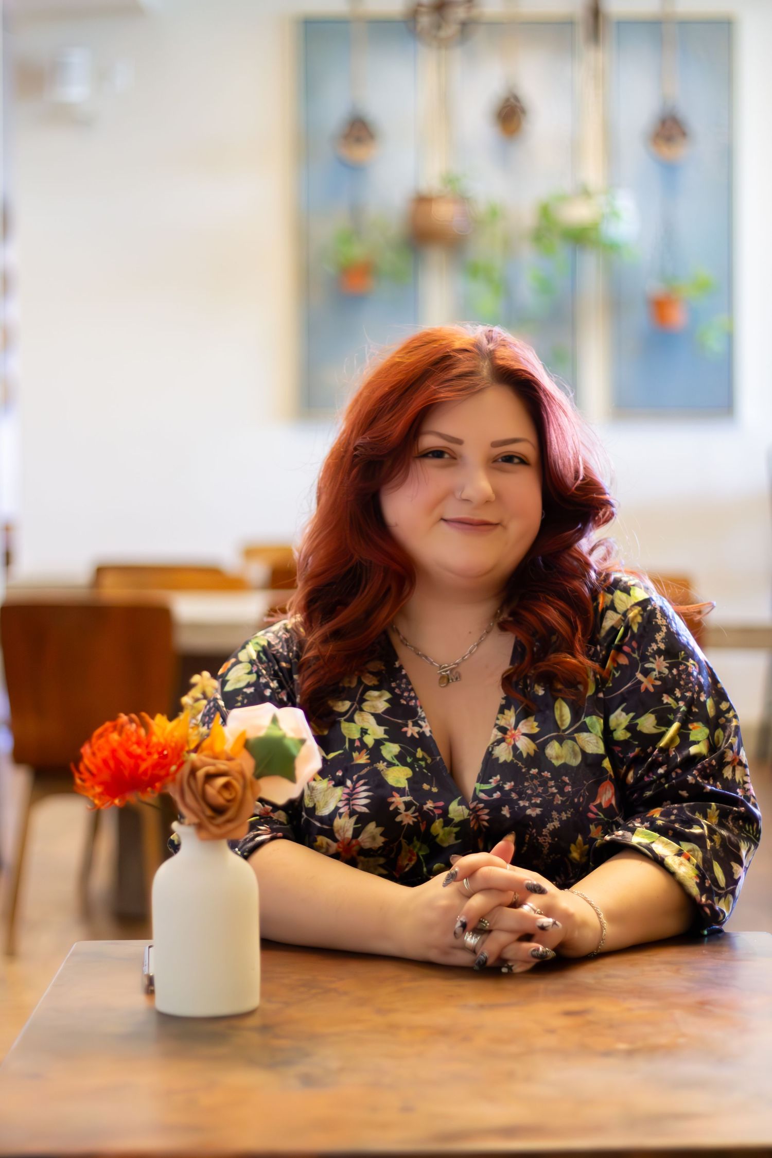 A person in a floral print dress relaxes at a wooden table with orange flowers and decor in the background.