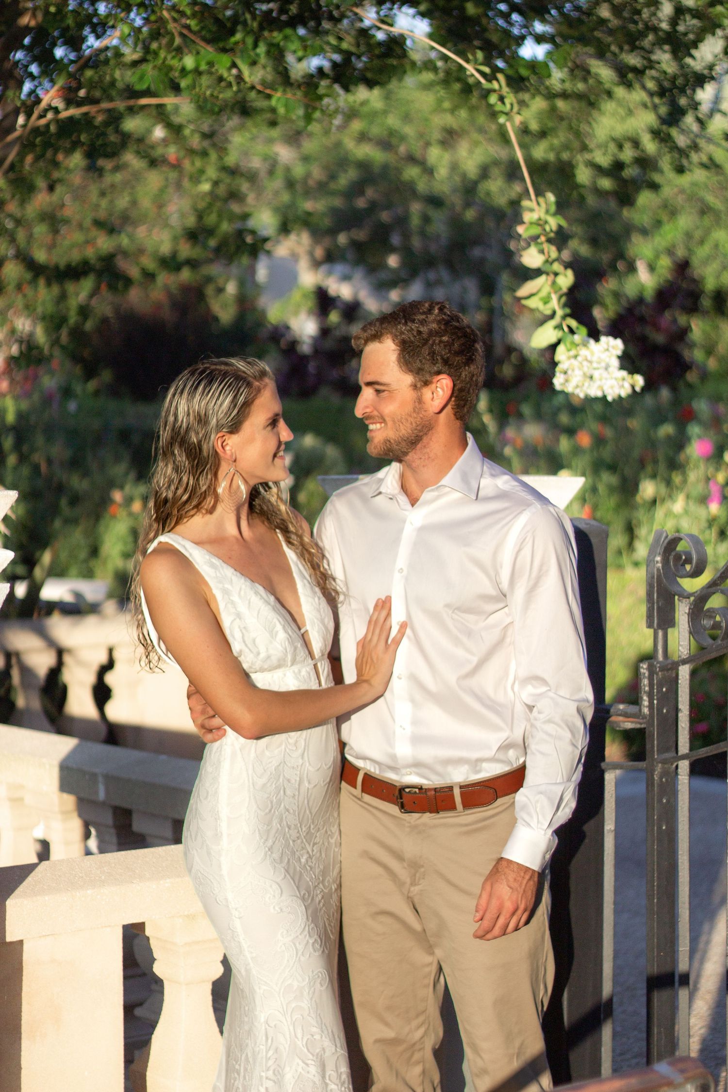 Couple in white dress and khakis poses playfully along stone fence outdoors.