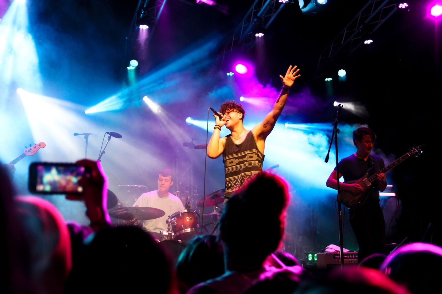 Concert performers on stage illuminated by vibrant purple and blue lighting effects during a live music performance.