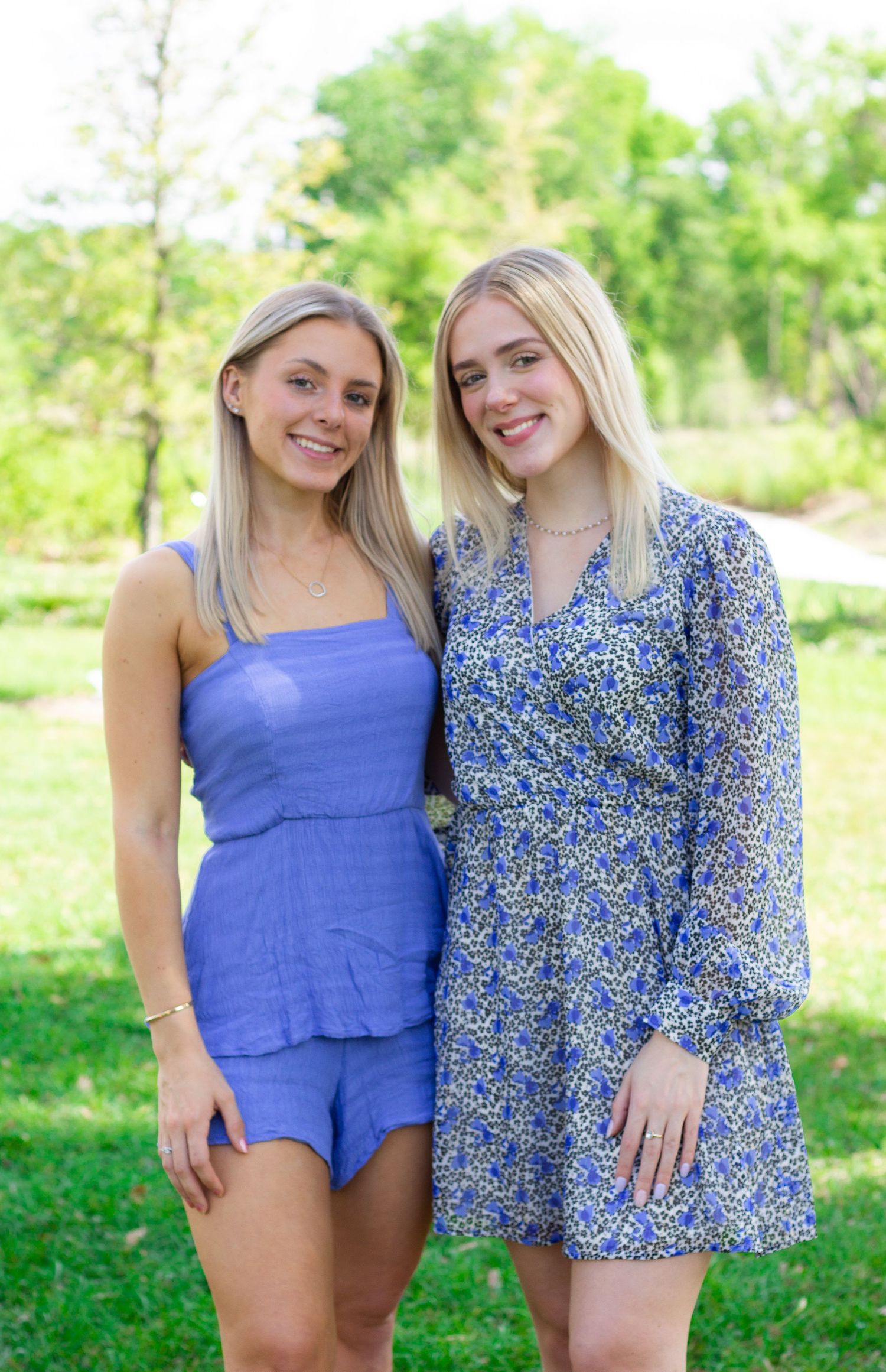 Two people in blue outfits posing outdoors in a sunny garden setting.