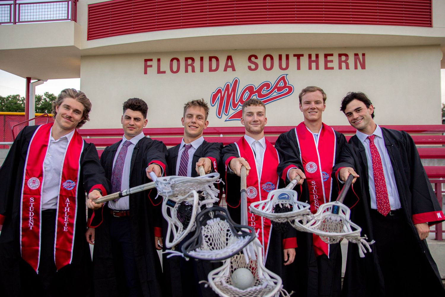 Group celebrating graduation with red Florida Southern stoles and ceremonial attire.
