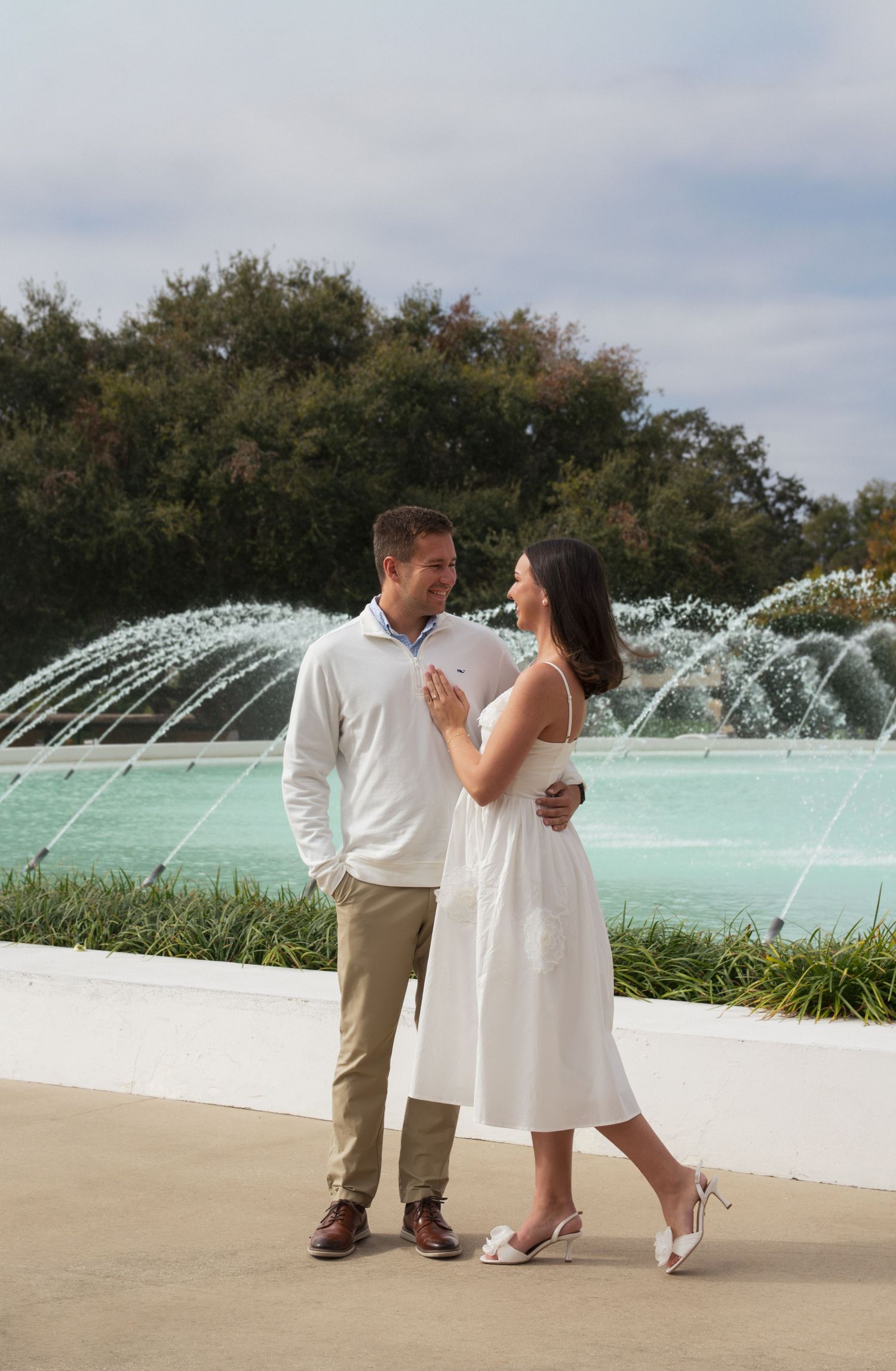 A couple stands together in front of a turquoise fountain display during a romantic outdoor photoshoot.