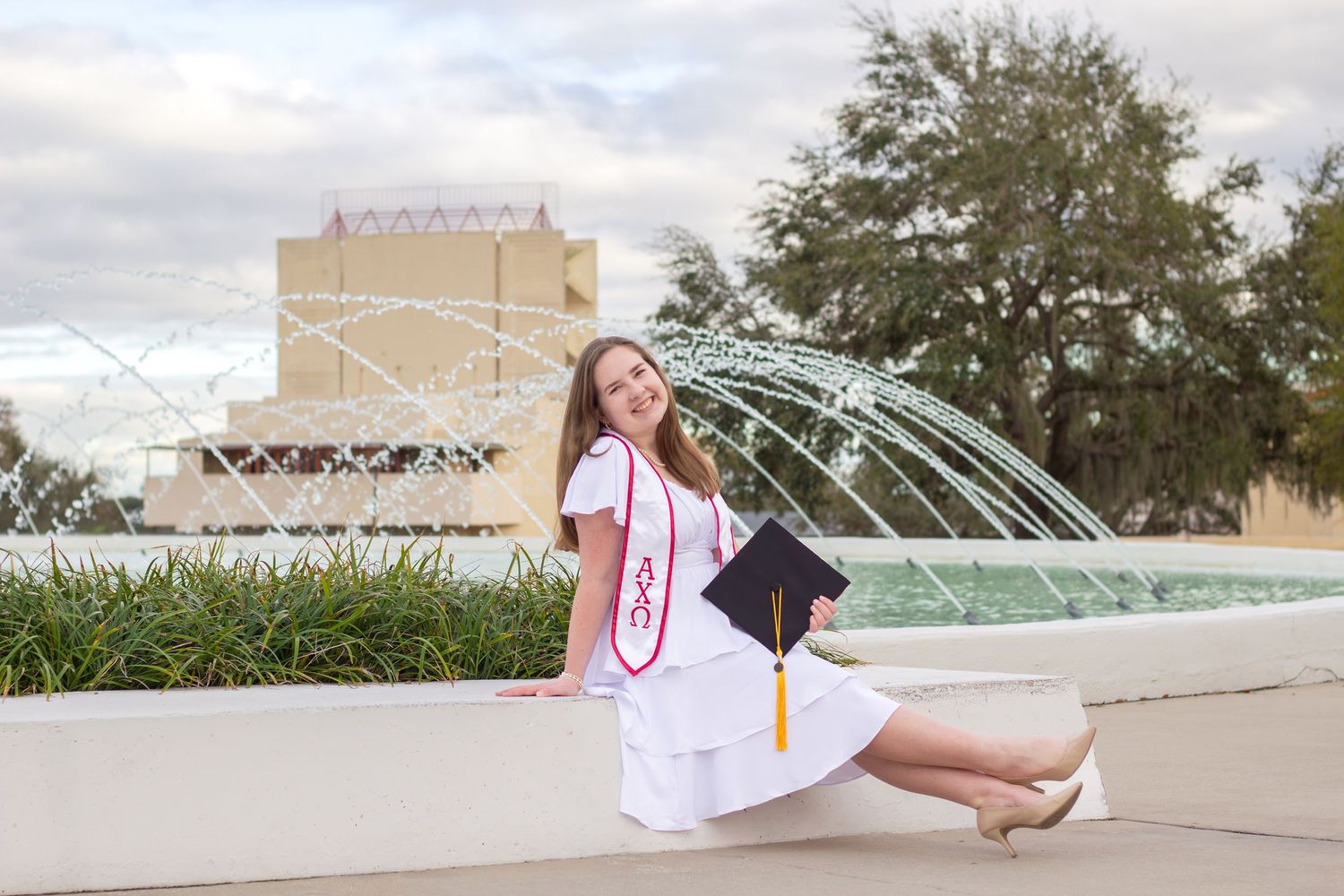 Graduate posing near water fountains at sunset on campus.