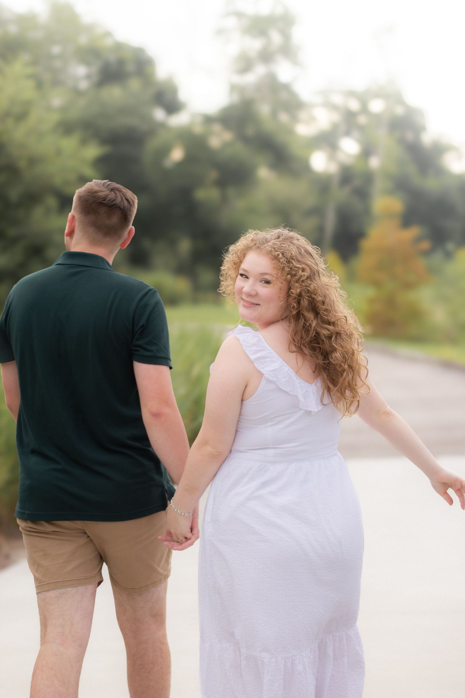 A joyful couple in casual attire dances and twirls together on a sunlit pathway.