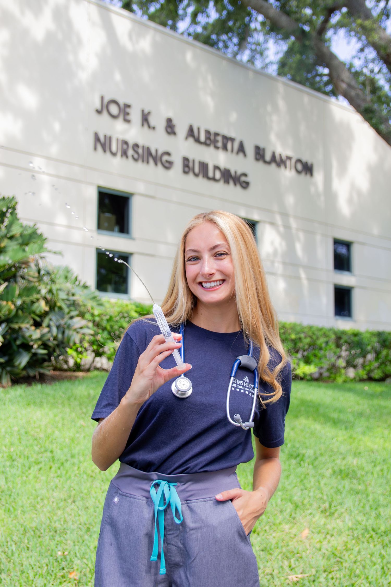 A nursing student in scrubs stands outside the Joe K. & Alberta Blanton Nursing Building with a stethoscope.