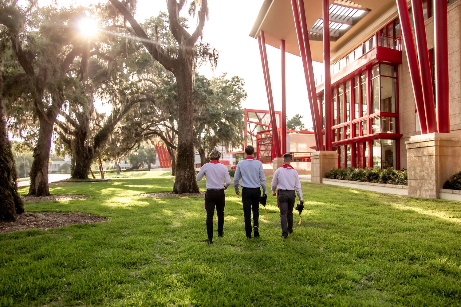 Group photo session on grassy hill with red architectural elements in background.