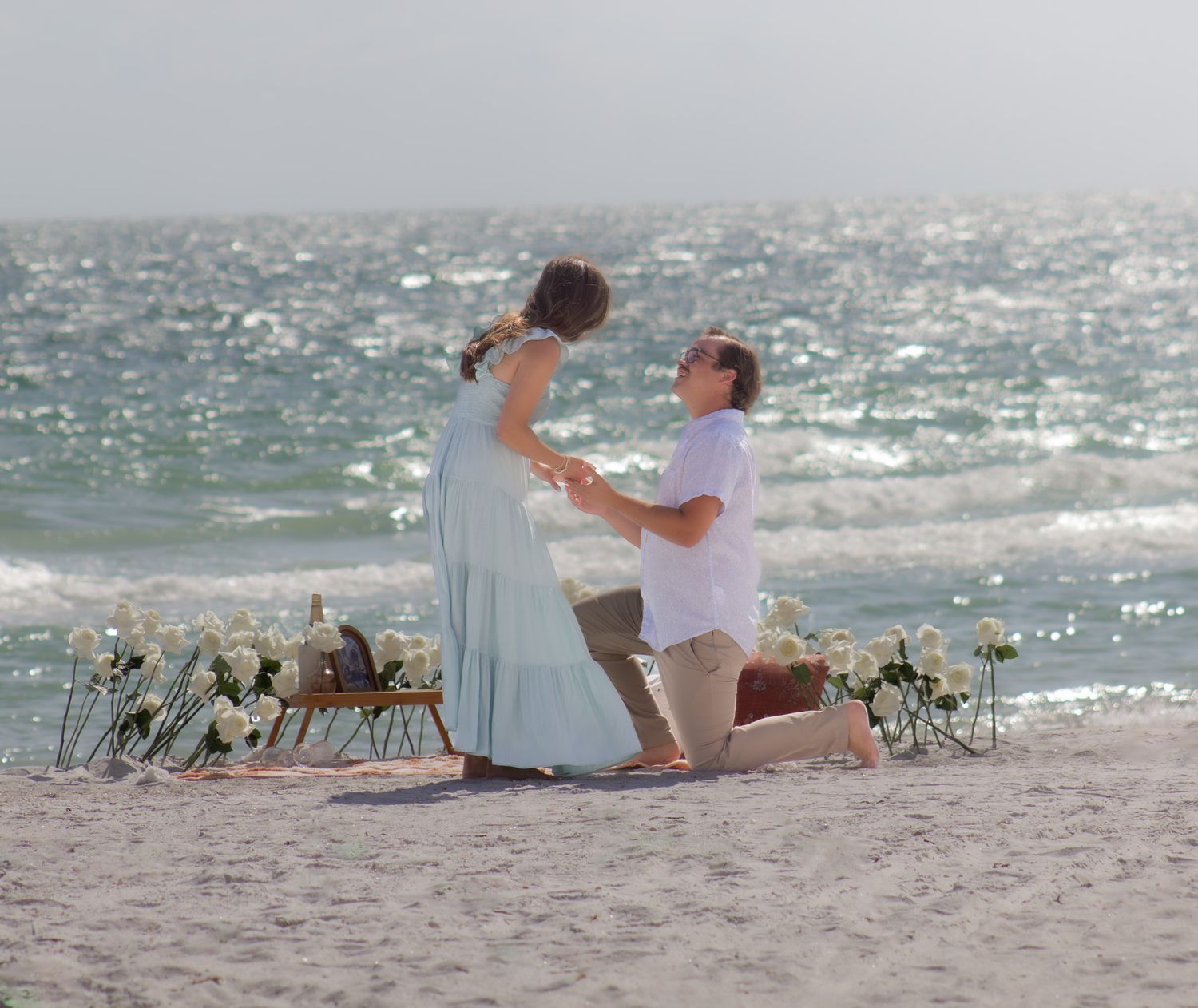 A romantic beach proposal setup with flowers and decor against the sparkling ocean.