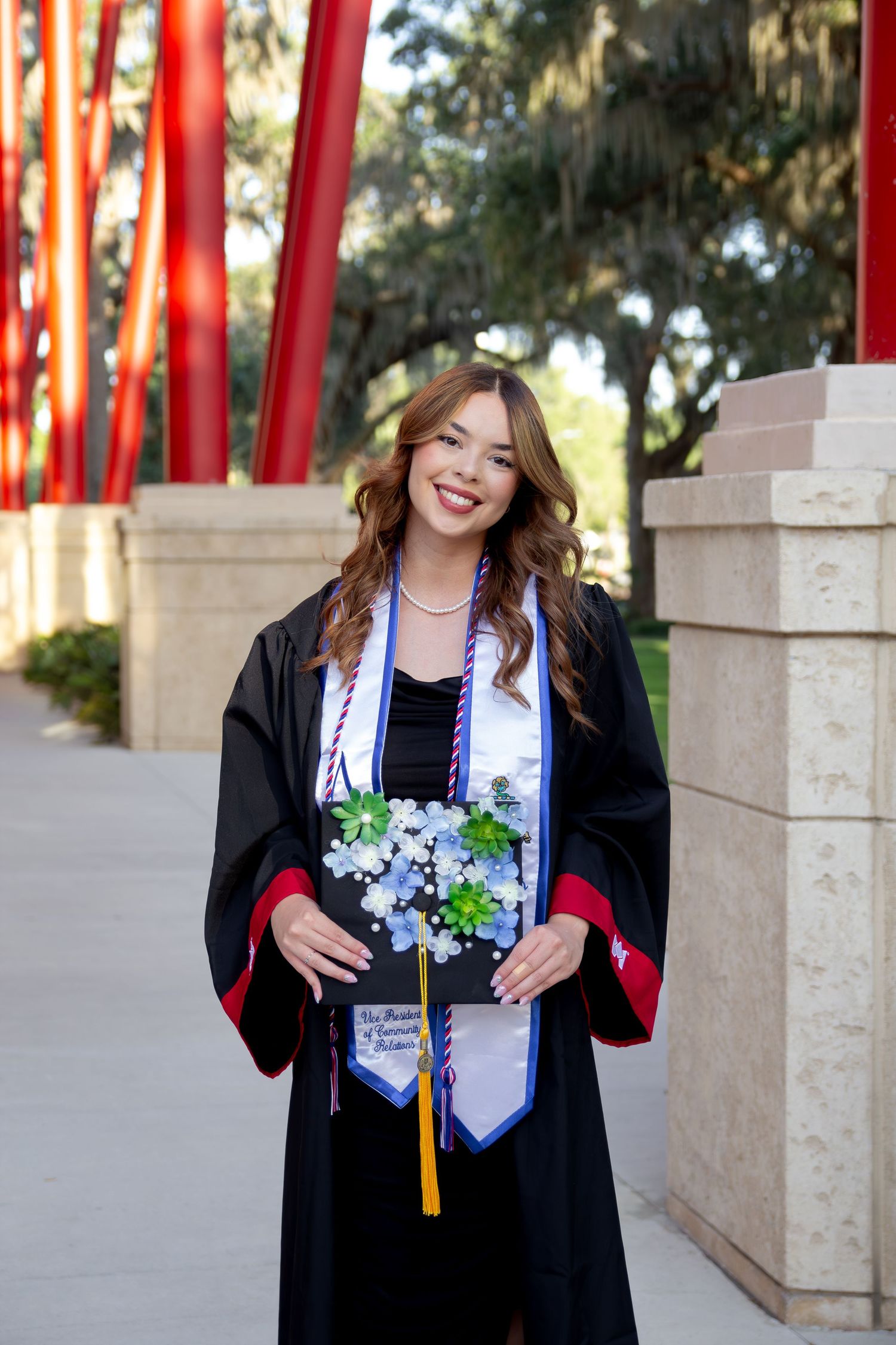 Graduate in black cap and gown celebrating with decorated stole and cords at graduation.