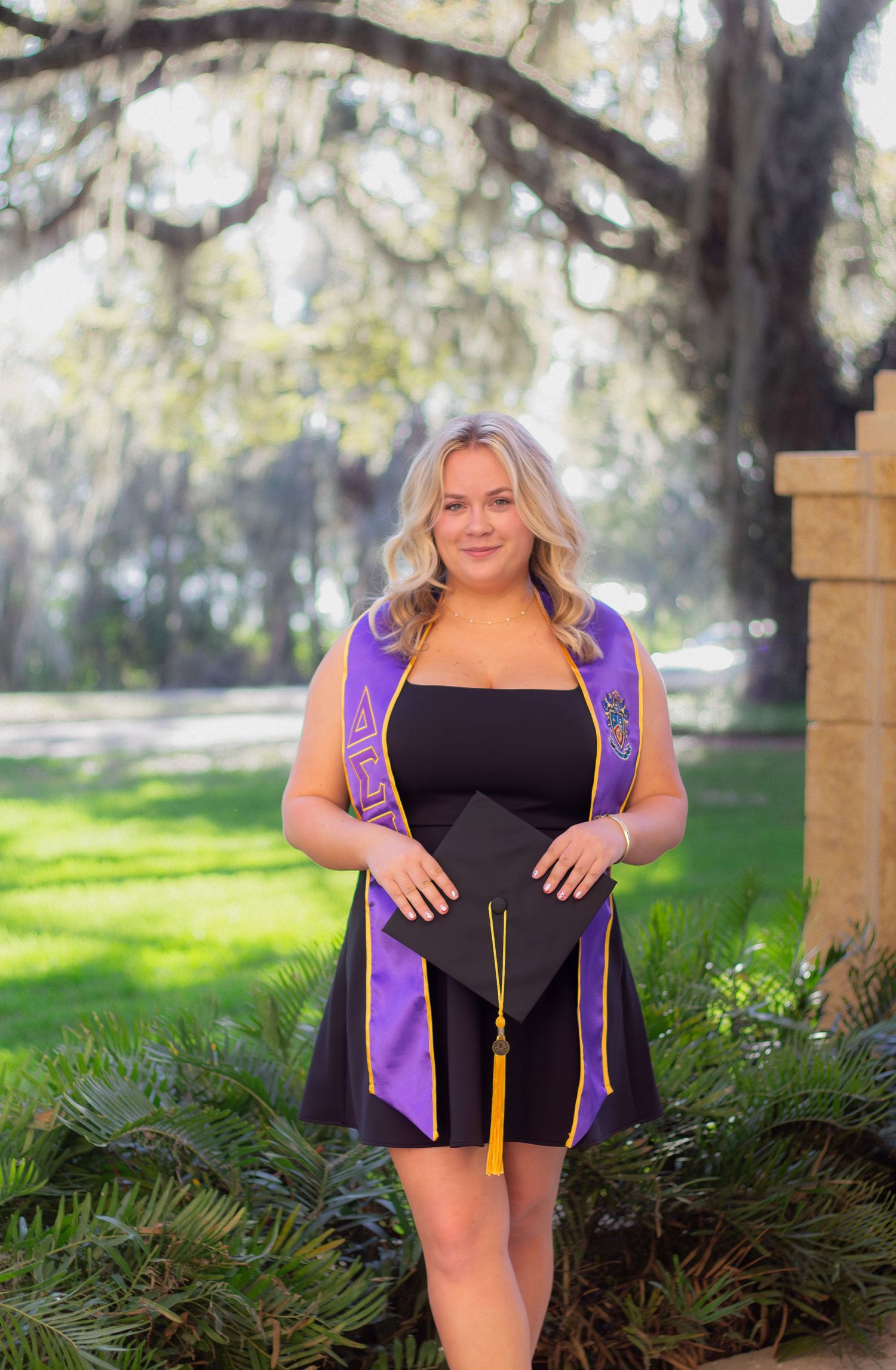 Graduation photos in purple academic regalia taken outdoors with Spanish moss trees.