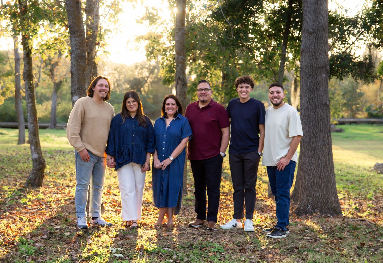 A group of people standing together outdoors among autumn trees and fallen leaves during golden hour.