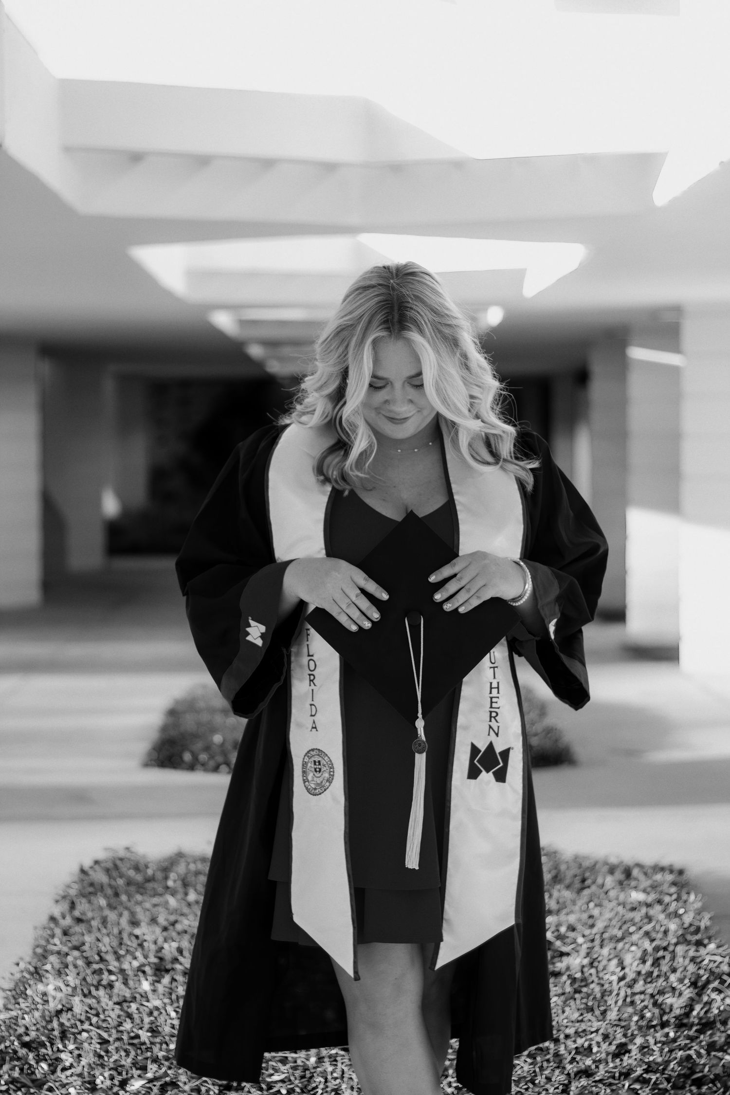Graduate in black cap and gown looks down at white stoles during outdoor graduation photo session.