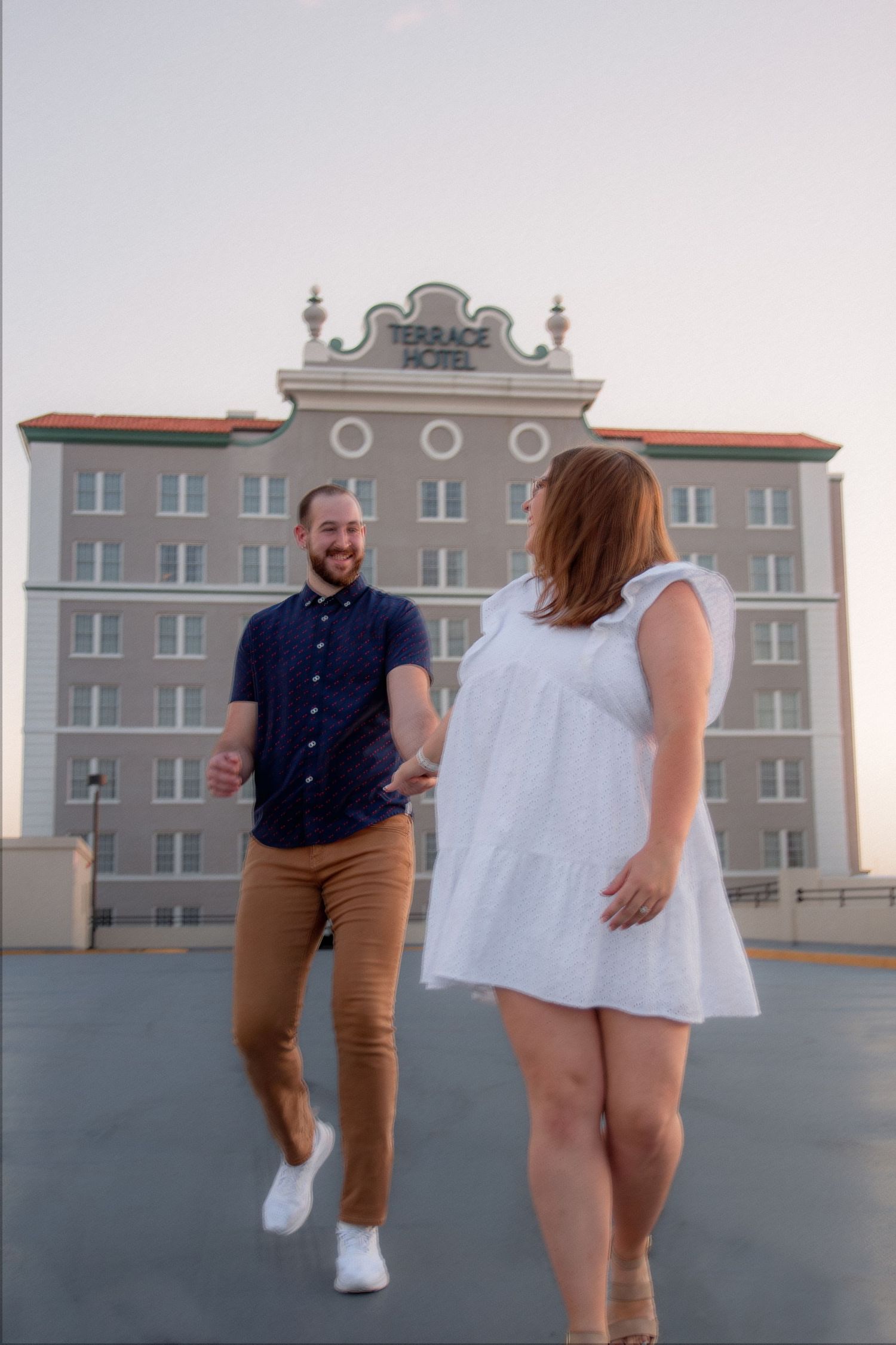 Two people dance joyfully together on a rooftop with city buildings visible in the background.