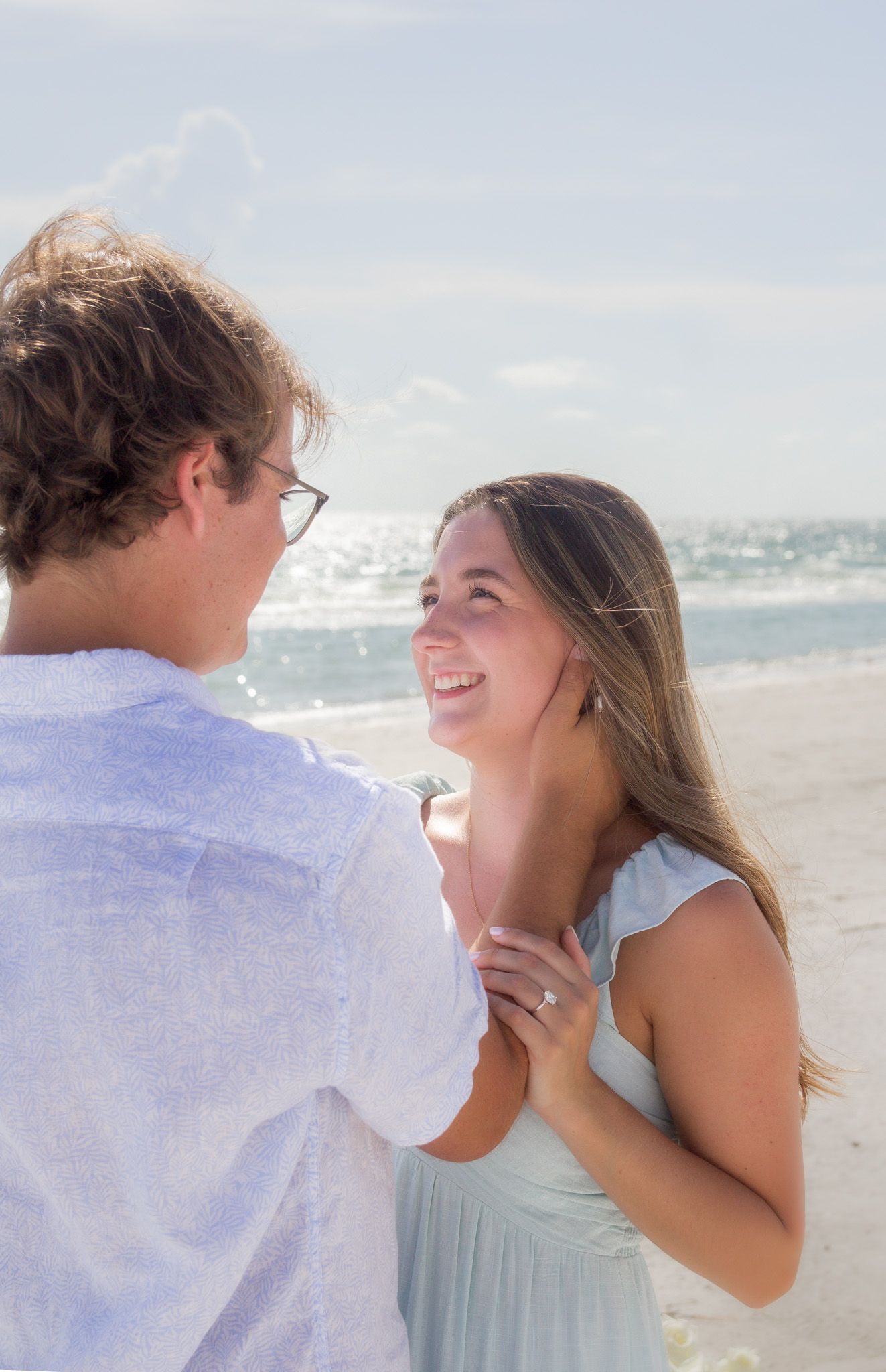 Two people laughing and embracing on a beach with ocean waves in the background.