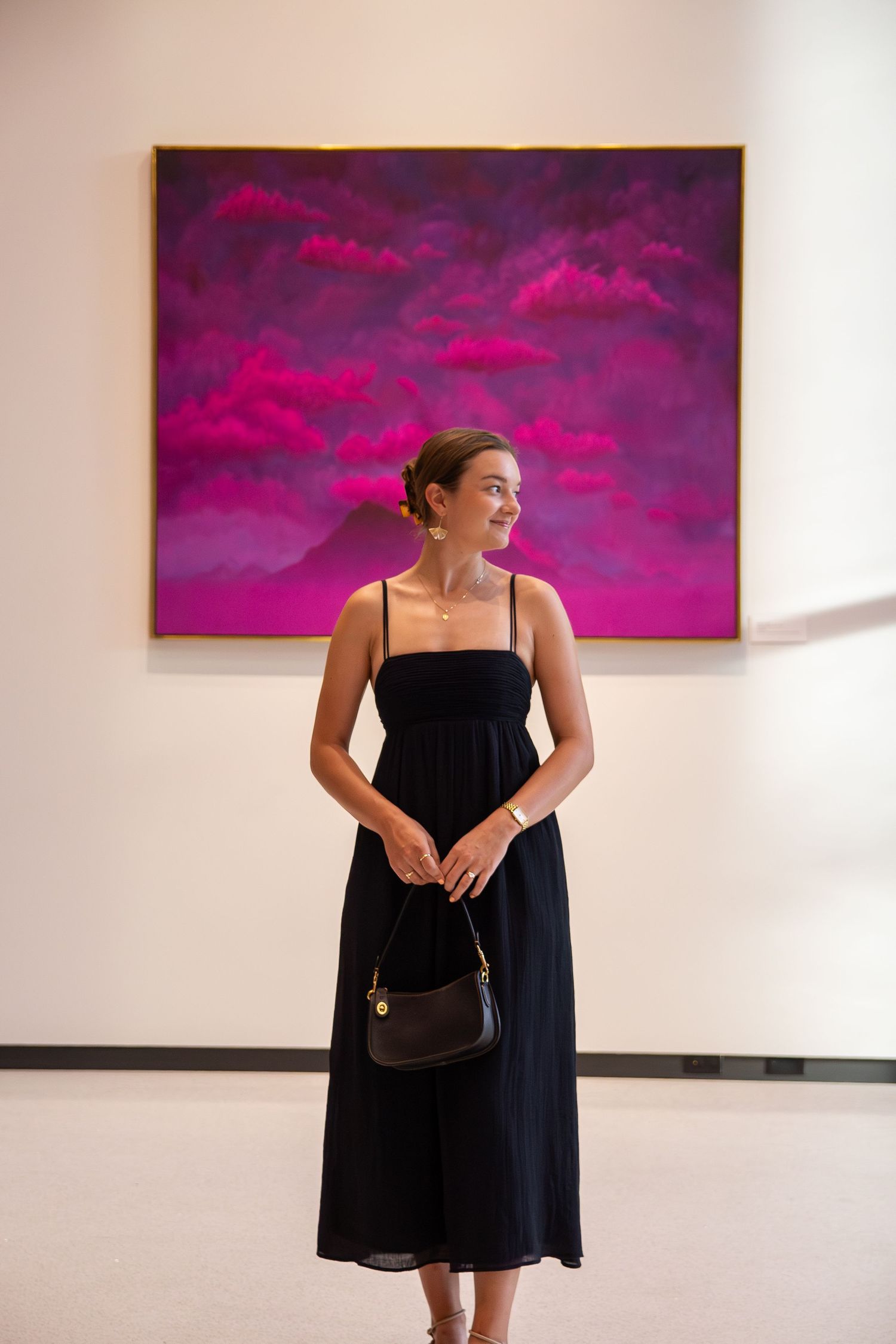 A series of fashion photographs showing someone in a black dress against white walls with vibrant pink artwork.