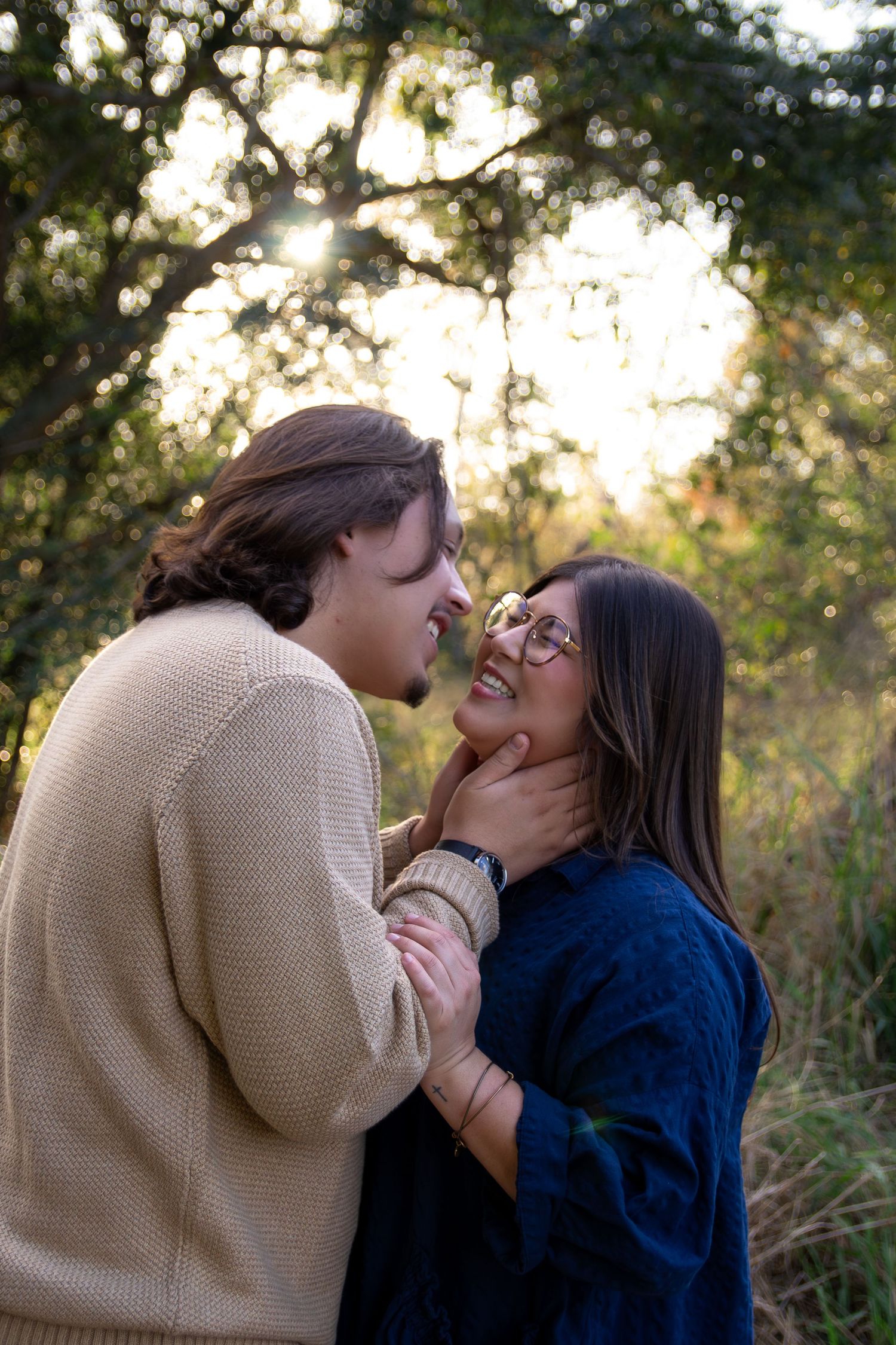 A couple laughs together outdoors during a romantic photoshoot at sunset in a natural setting.