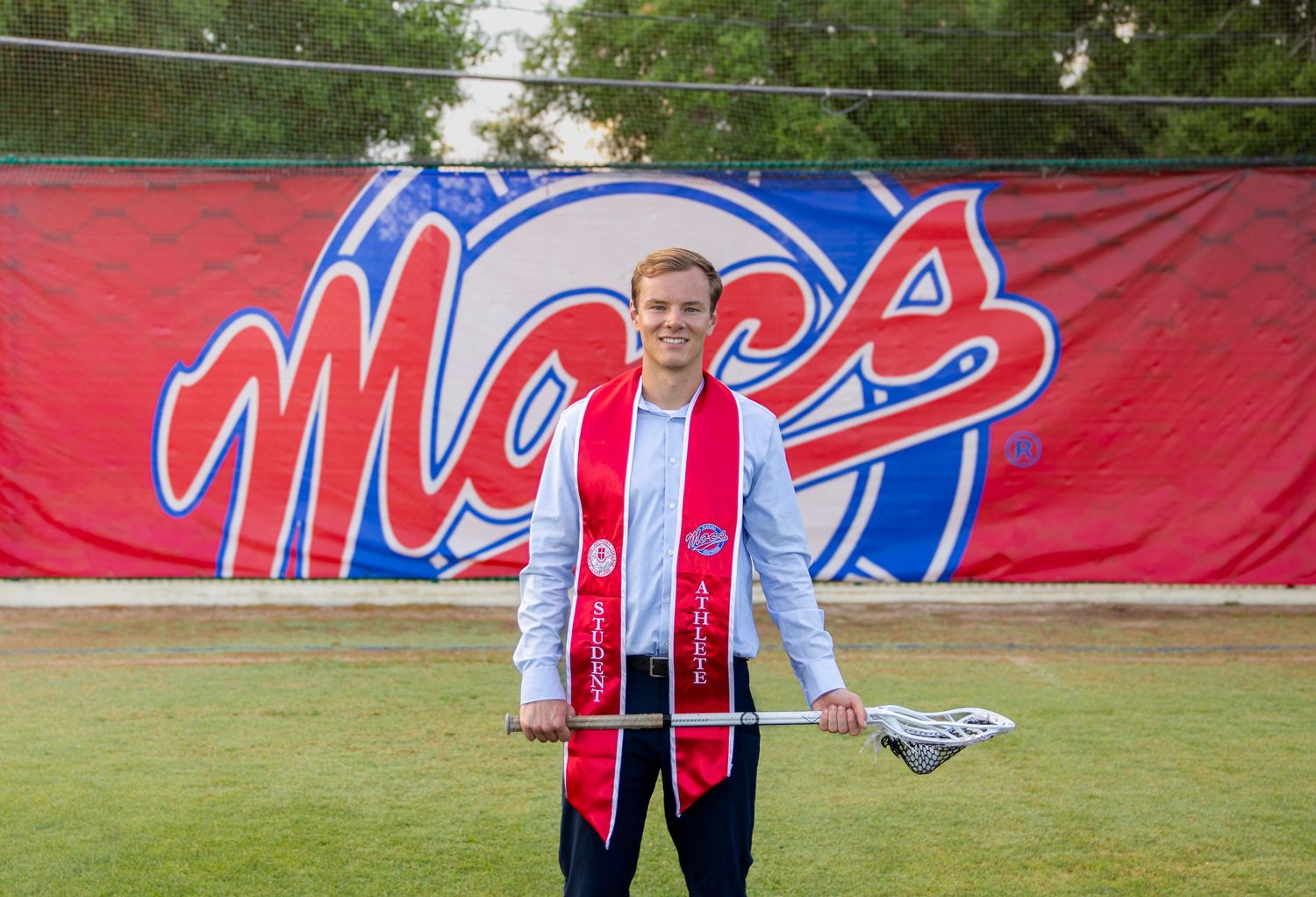 Graduates in red stoles posing with university backdrop during commencement.