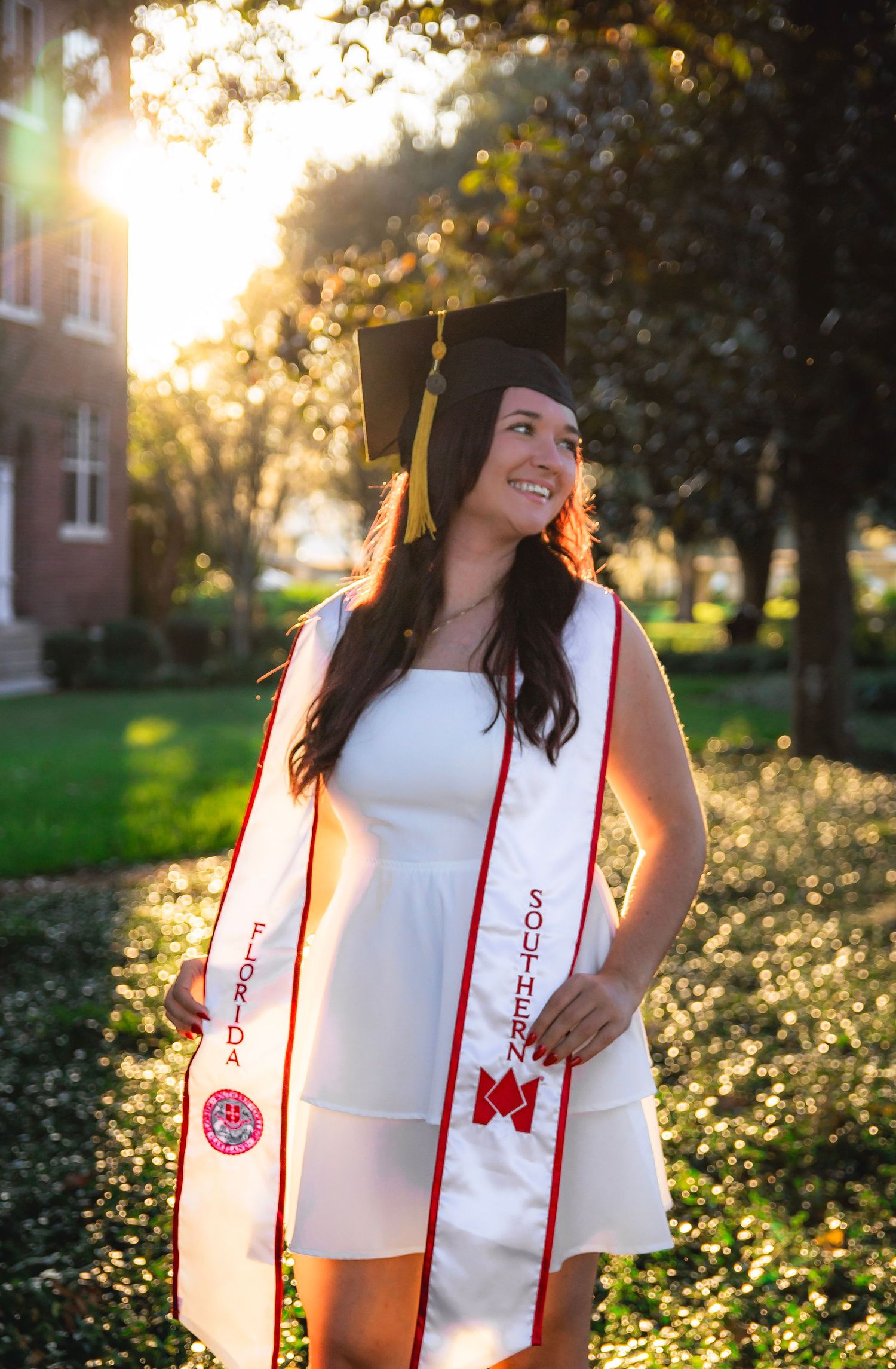 A graduation stole with red trim and decorative emblems glows in golden sunlight against a background of blooming flowers.