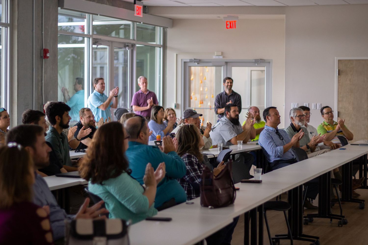 Students attend a classroom presentation while seated at long tables in a modern educational facility.