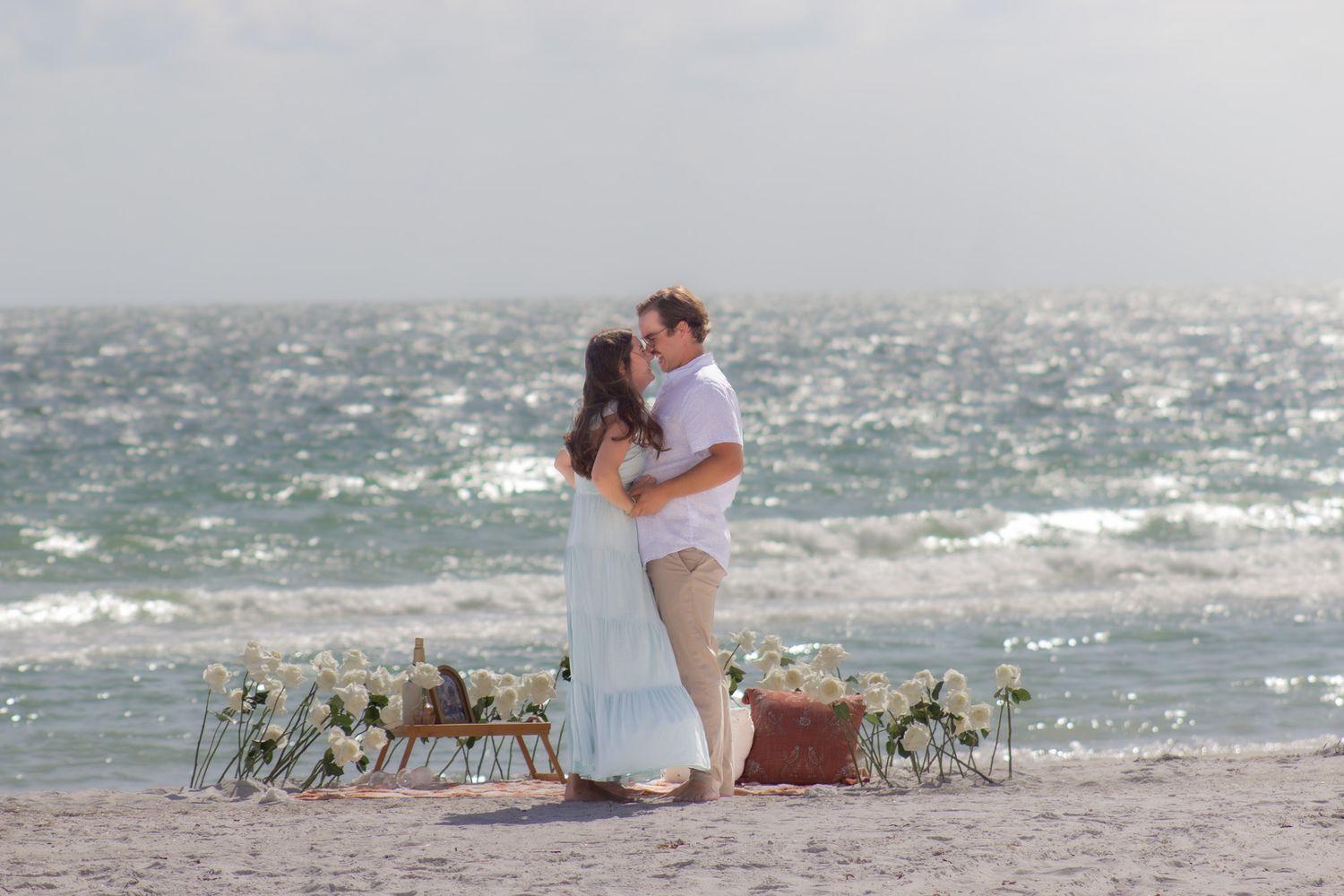 Romantic beach proposal moment captured during sunset with ocean waves in background.