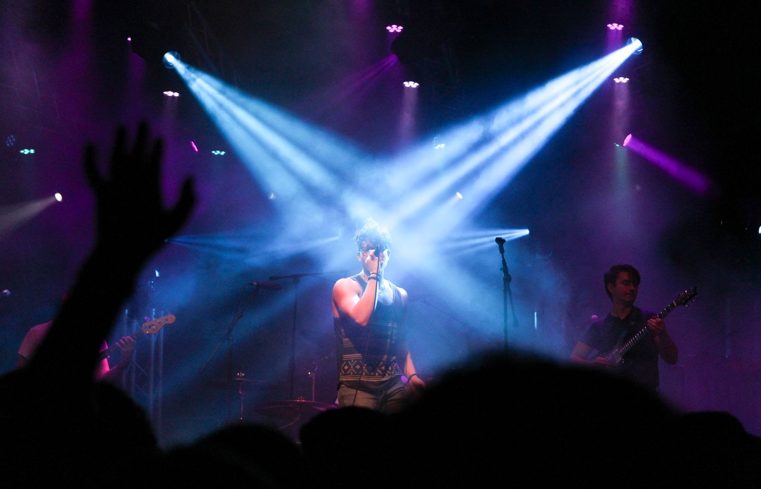 Concert stage illuminated with dramatic purple and blue spotlights creating atmospheric lighting effects during performance.