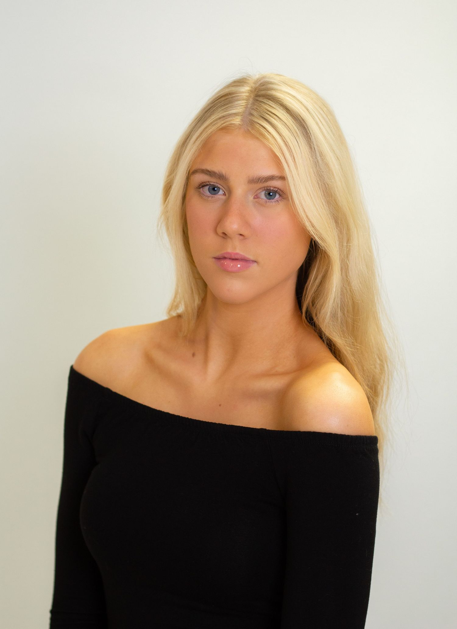 Professional studio portrait against white background featuring off-shoulder black top.