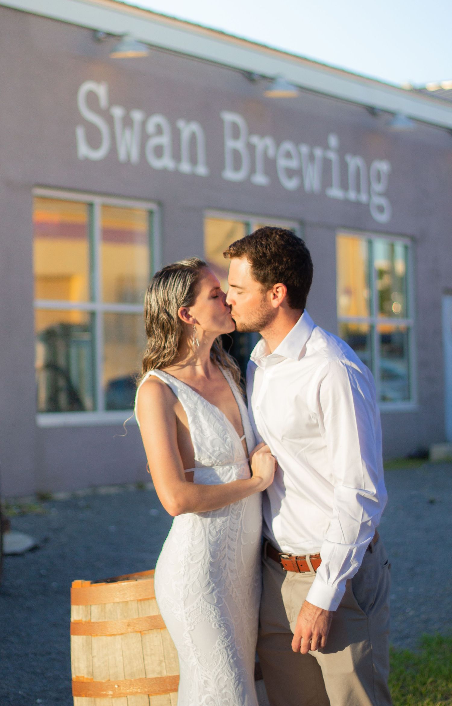 Couple shares intimate moment outside Swan Brewing building in wedding attire.