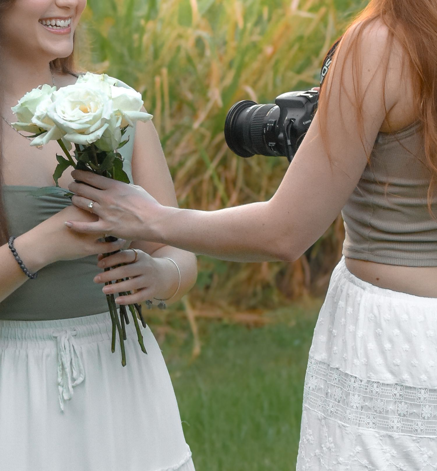 Two people exchanging white roses while wearing summer dresses outdoors.