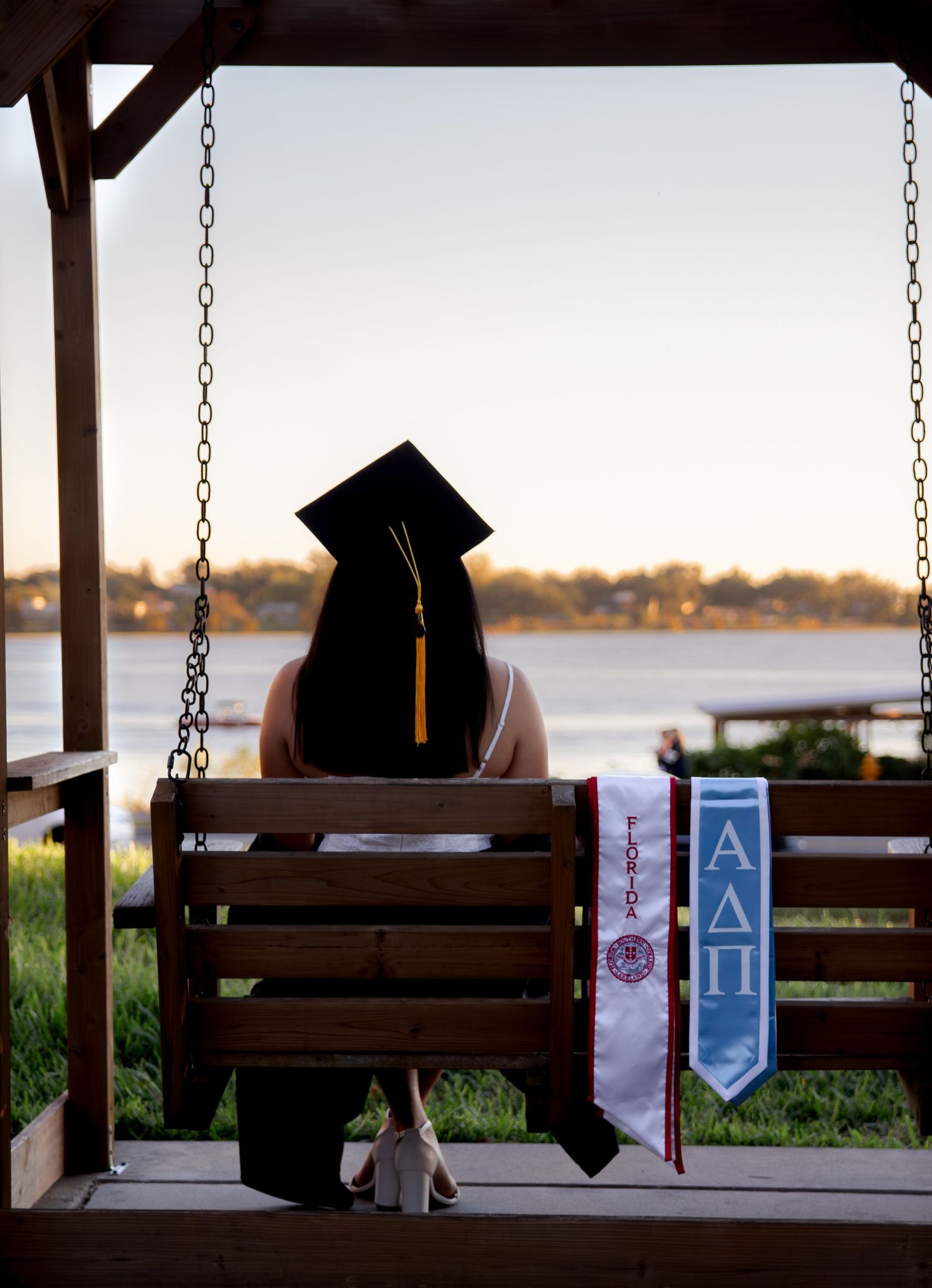 Three wooden swings on a covered porch overlook a serene waterfront view at sunset.