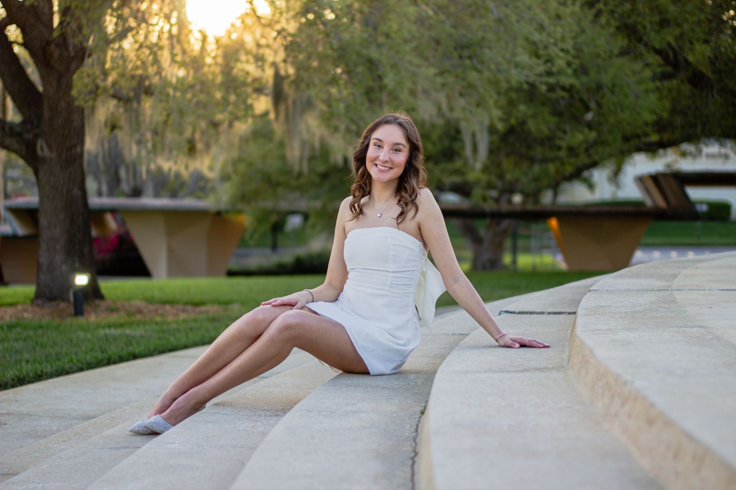 A bride in a white wedding dress poses gracefully on stone steps during a golden sunset photoshoot.
