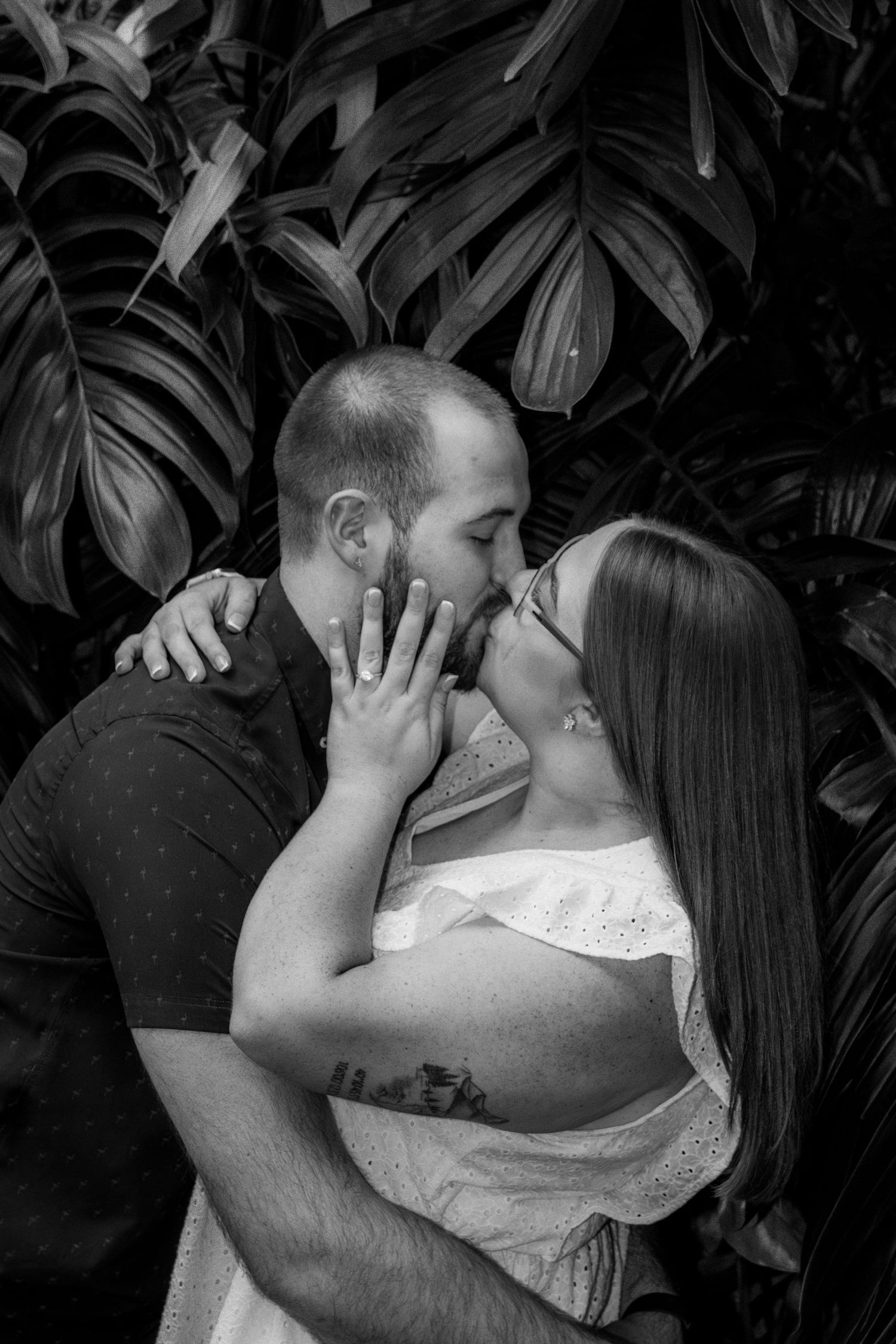 Black and white intimate portraits of couple sharing tender kisses against tropical foliage backdrop.