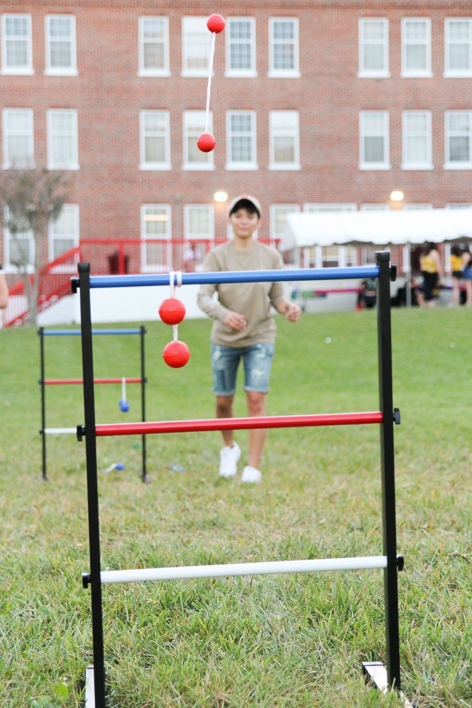 Red balls hover above white and blue poles set up on grass with brick buildings in the background.