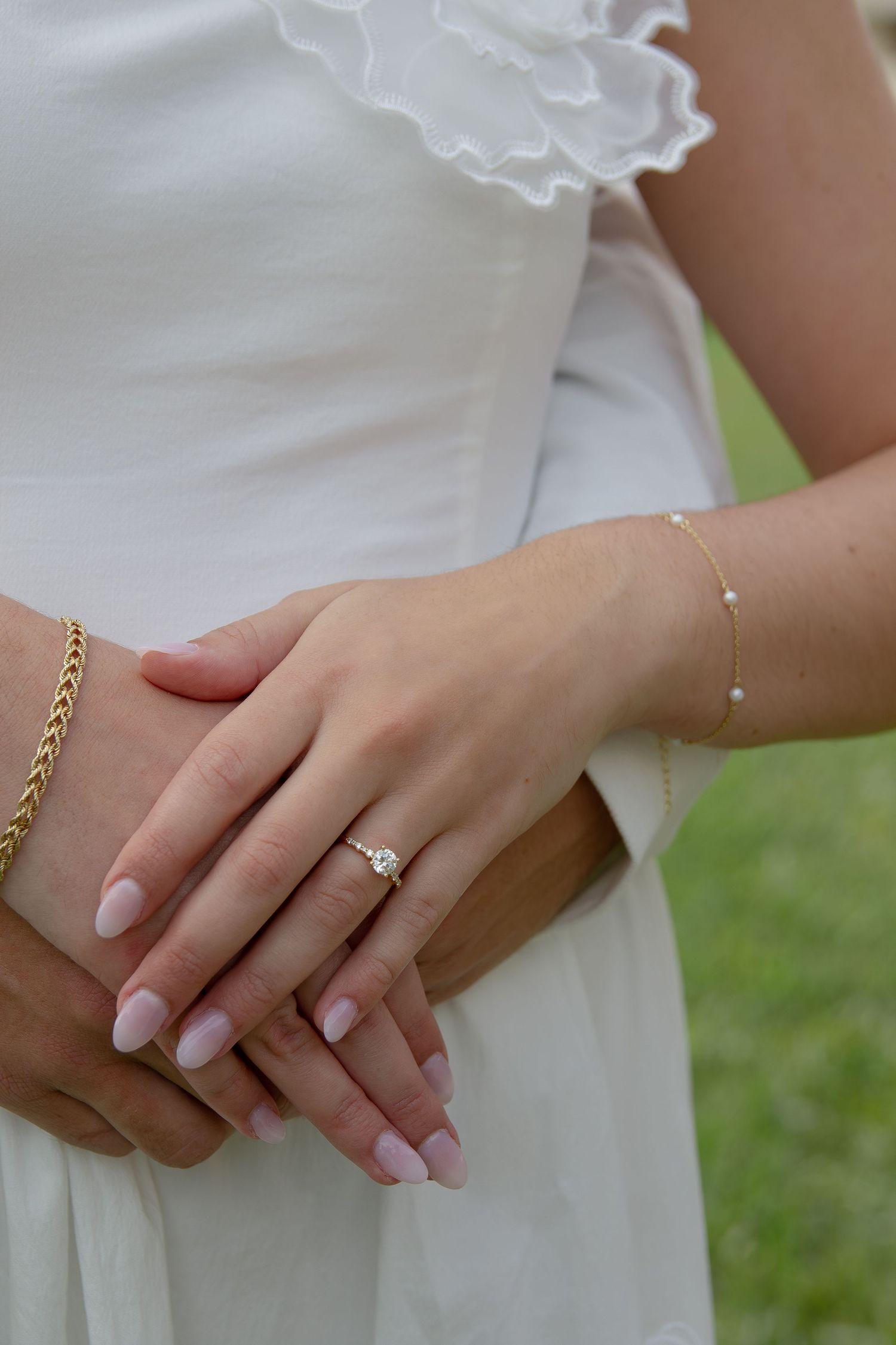 Close-up of hands showing an engagement ring on a finger with white dress and gold bracelet details.