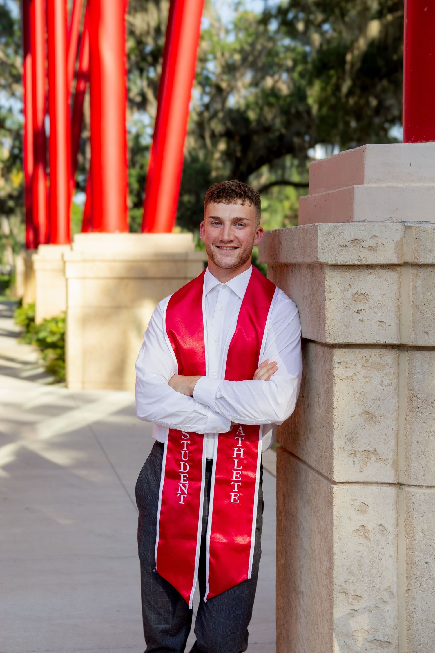 Graduate in red stole posing by architectural columns at Florida Southern.
