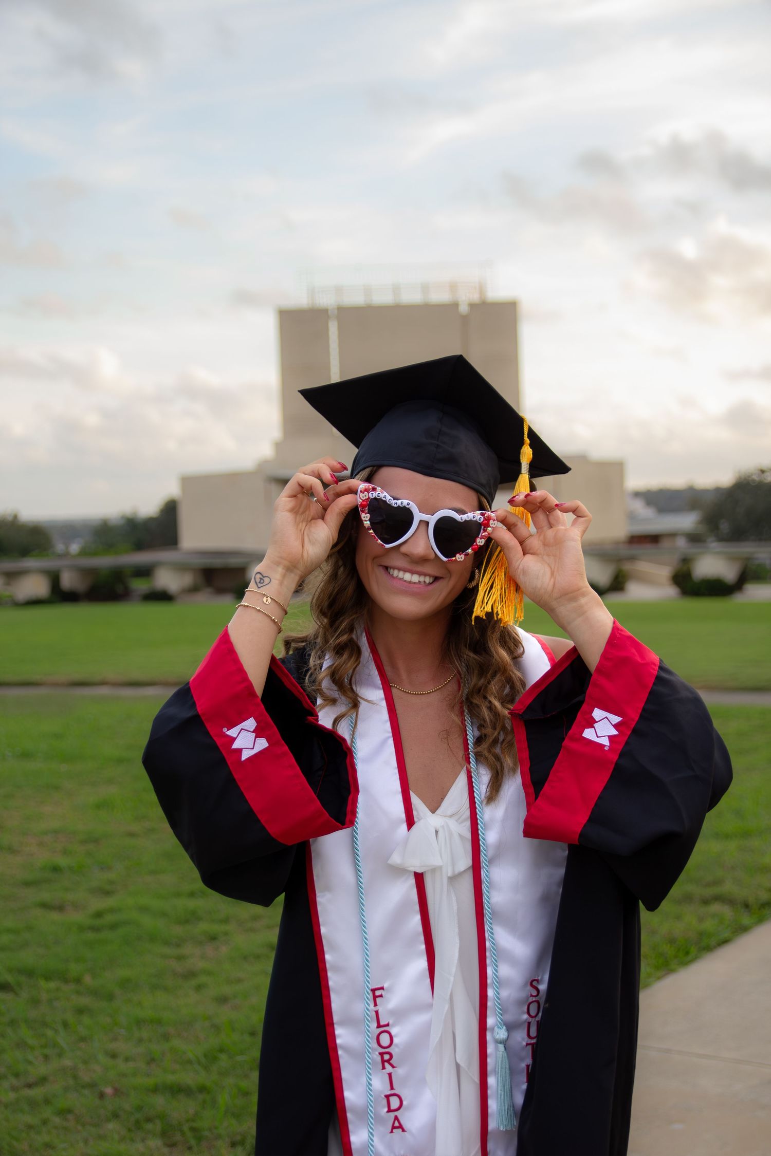 A graduate in a black cap and gown and white sunglasses poses playfully in a series of outdoor photos.