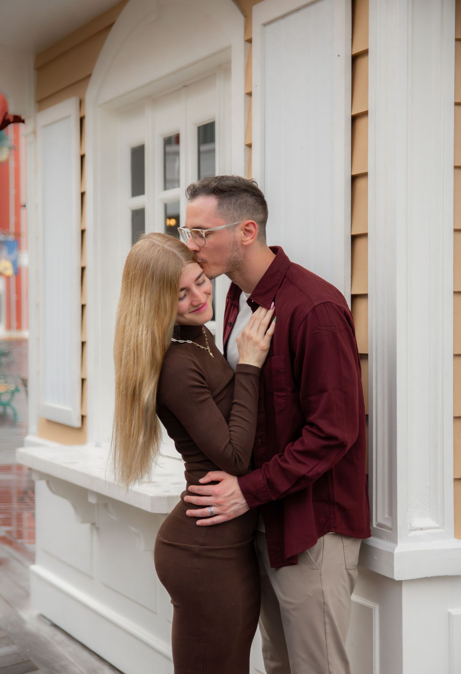 A couple shares an intimate moment while standing against a white building exterior.