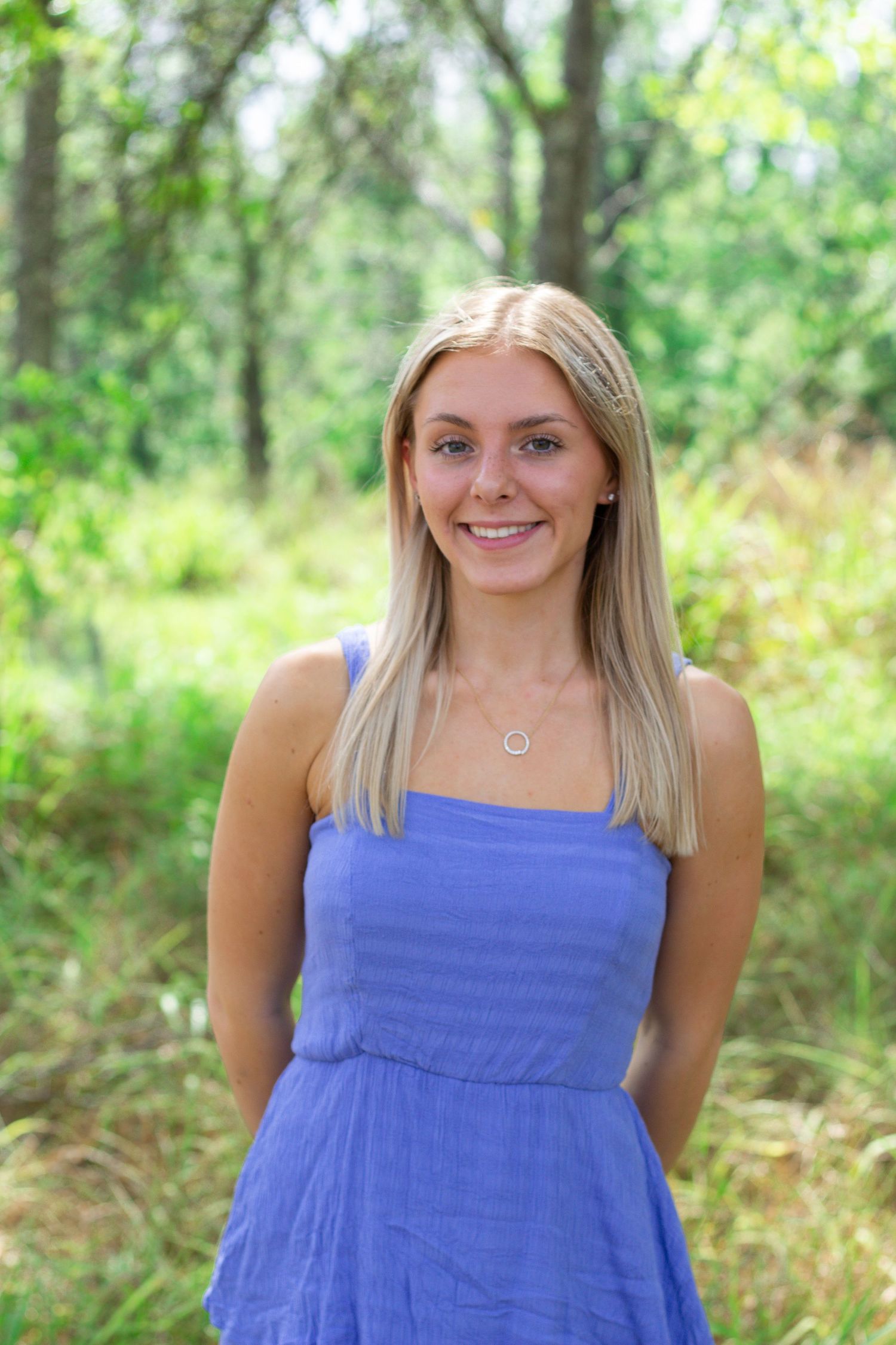 Person in blue summer dress standing in natural outdoor setting with green foliage.