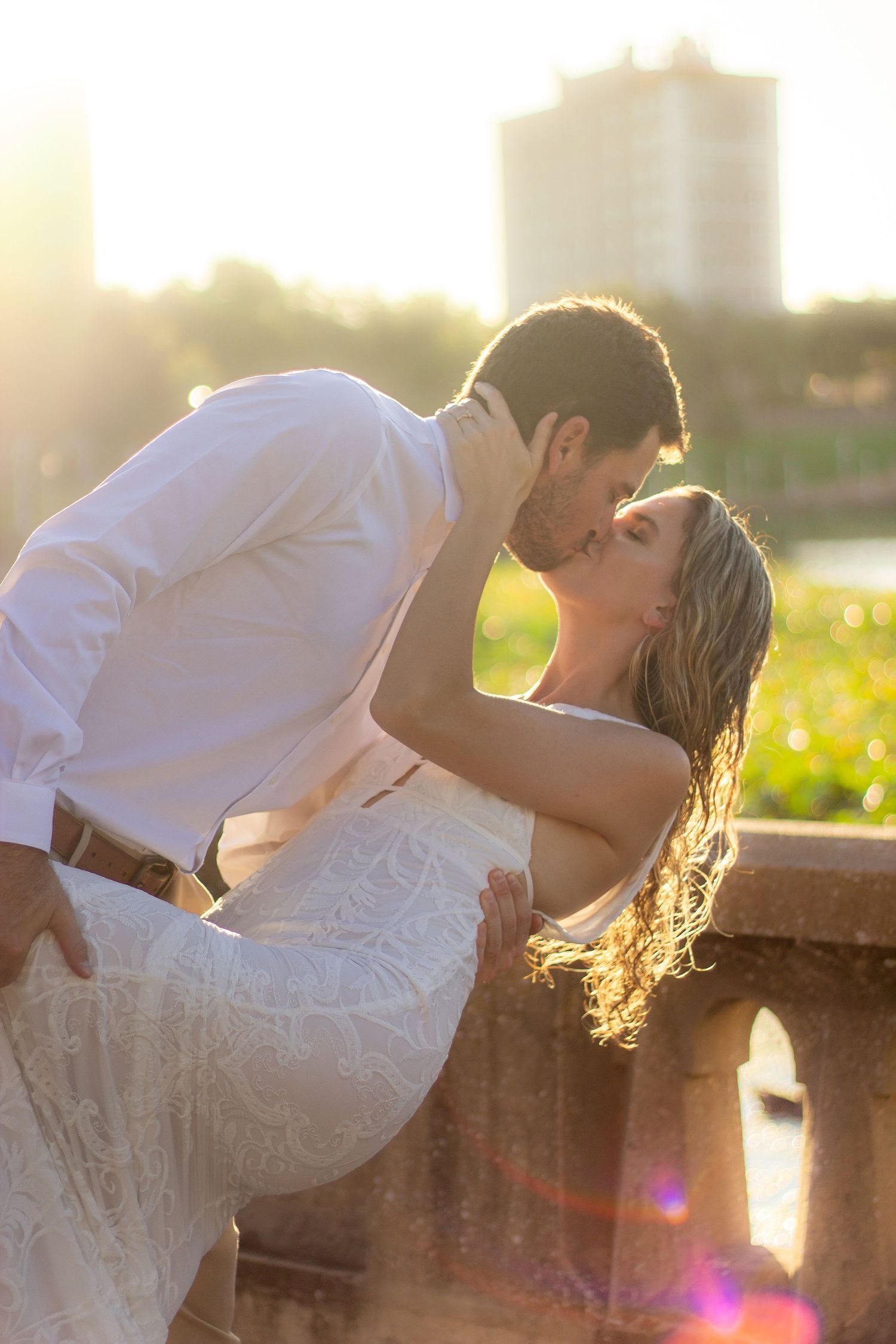 Romantic sunset photoshoot with couple kissing against stone railing in golden light.