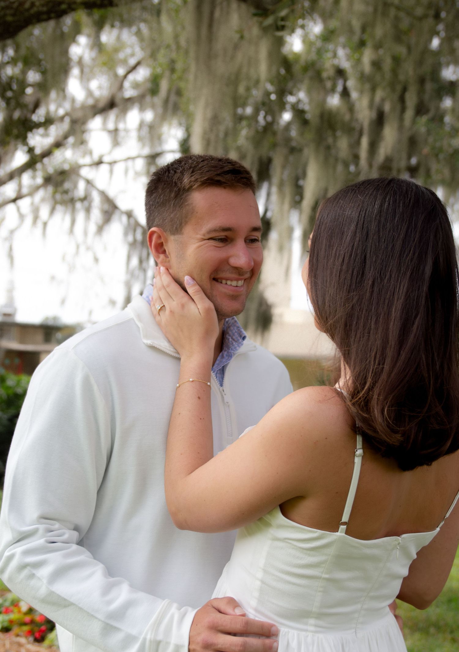 A romantic couple shares joyful laughter together during an outdoor photo session under moss-draped trees.