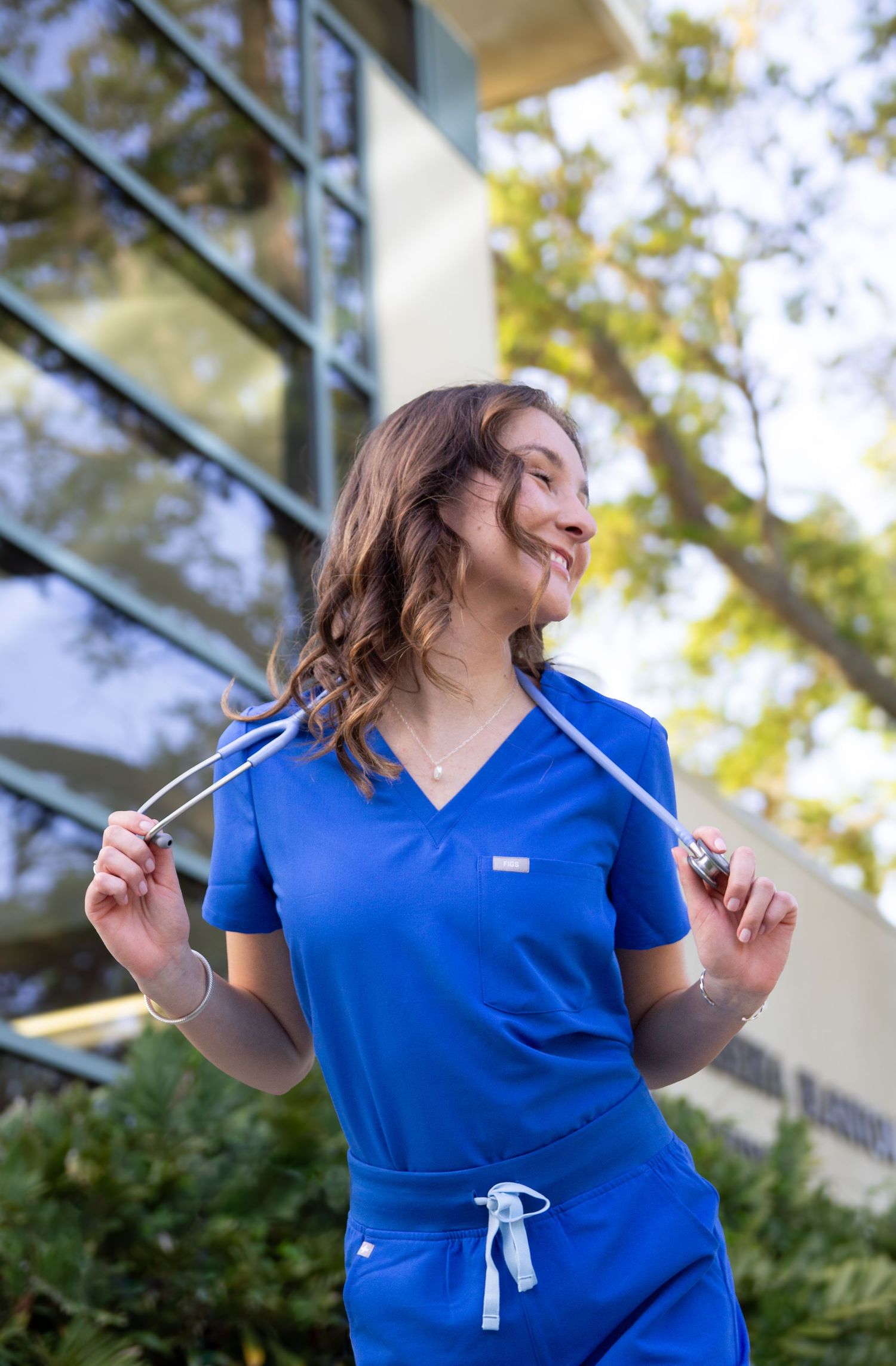 Healthcare worker in blue scrubs smiling and moving outdoors on a sunny day.