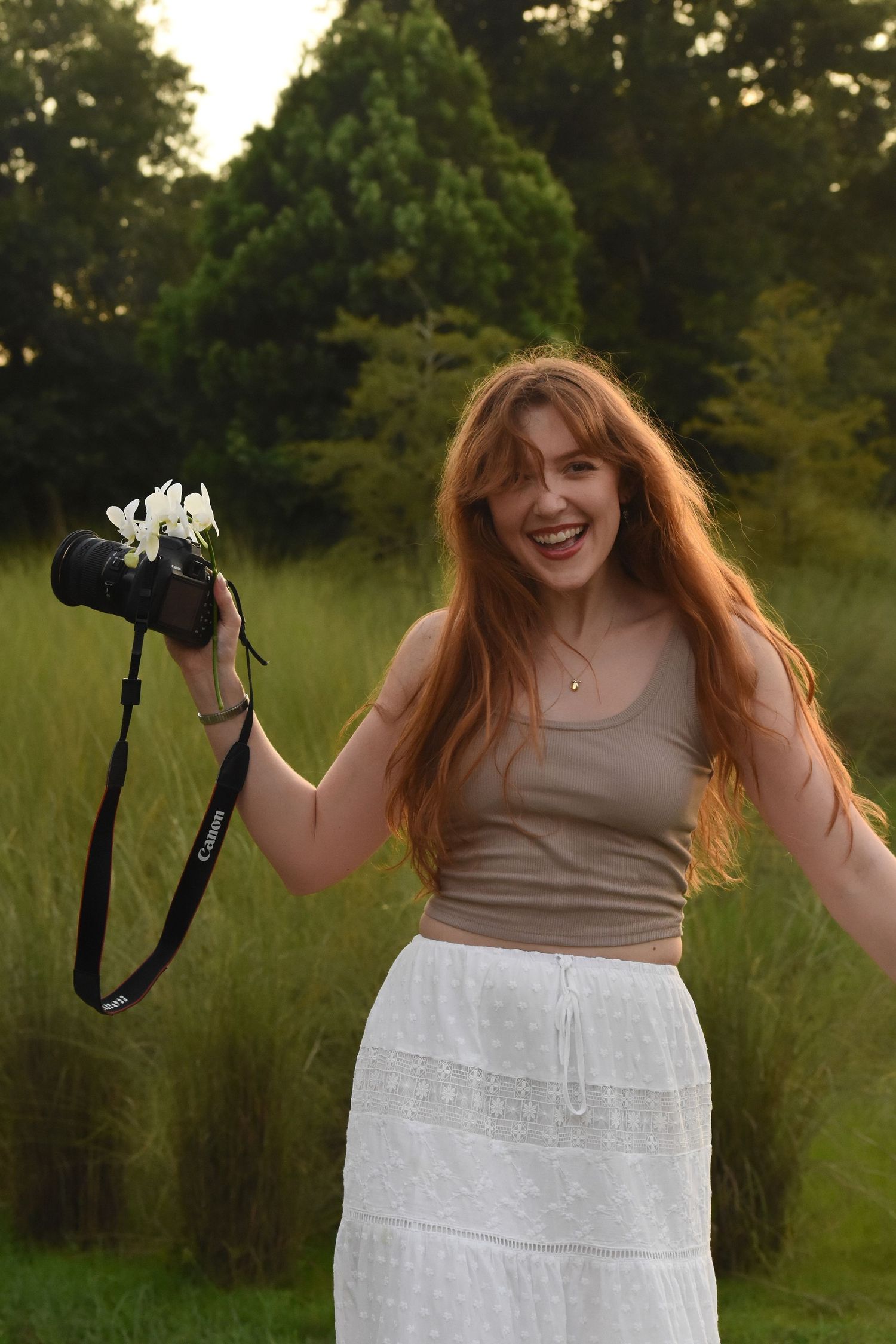 Alexis with Lex & Light Co. wearing a tan top and white dress twirls joyfully in a green field at sunset.
