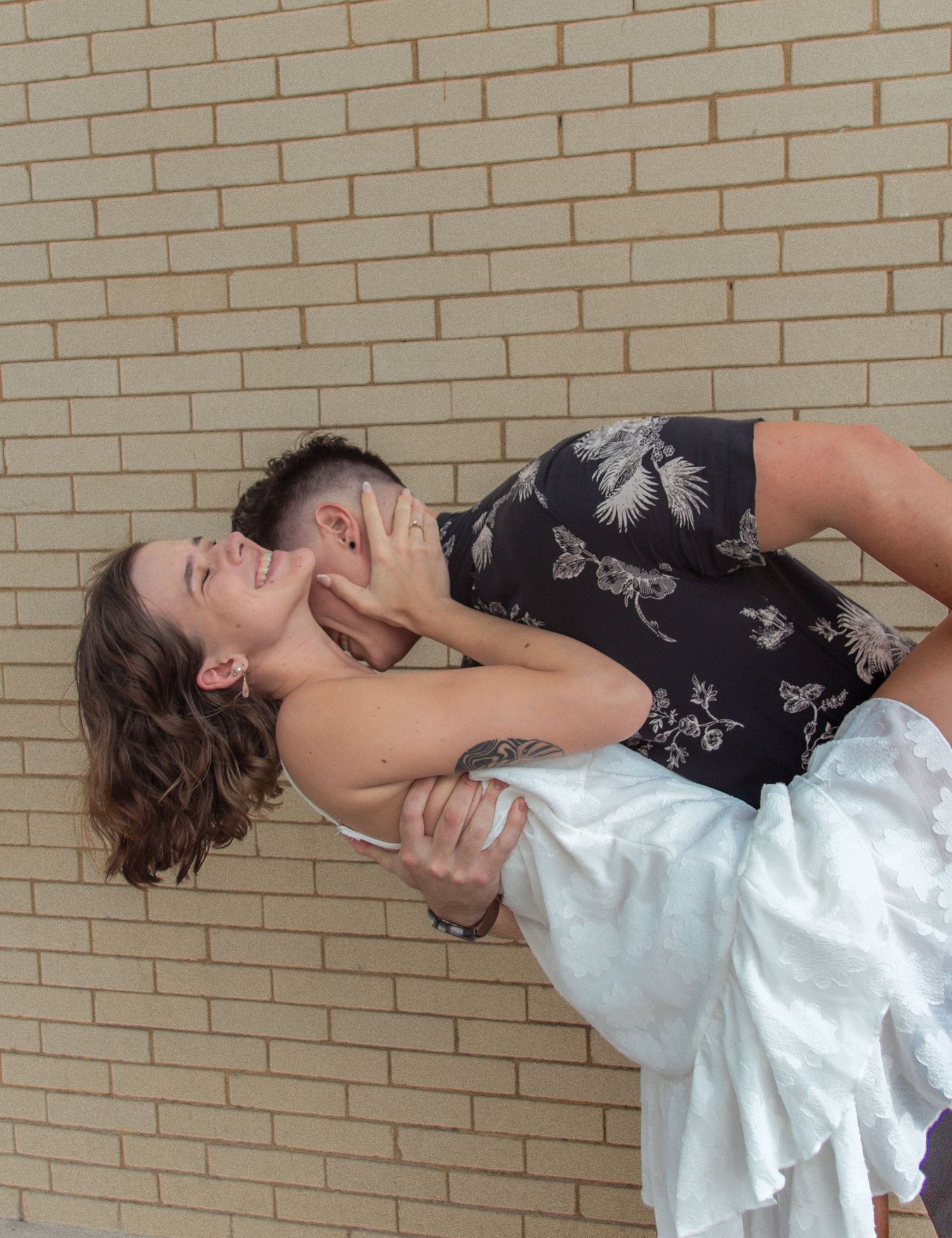 Couple lying against brick wall in playful pose.