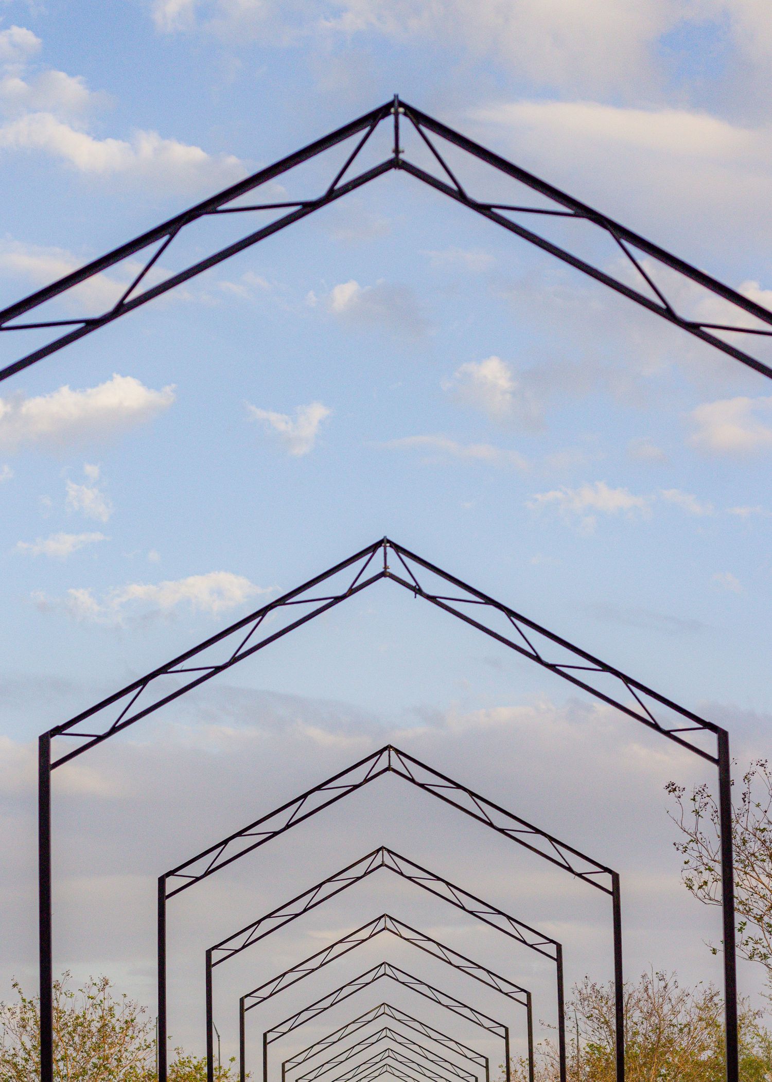 Geometric architectural beams create a repeating pattern against a blue sky with white clouds.