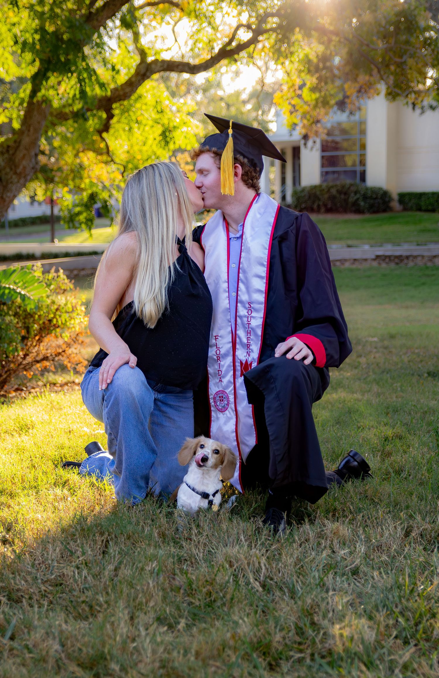 Graduation photo session in a grassy field with a small dog joining the outdoor portraits.