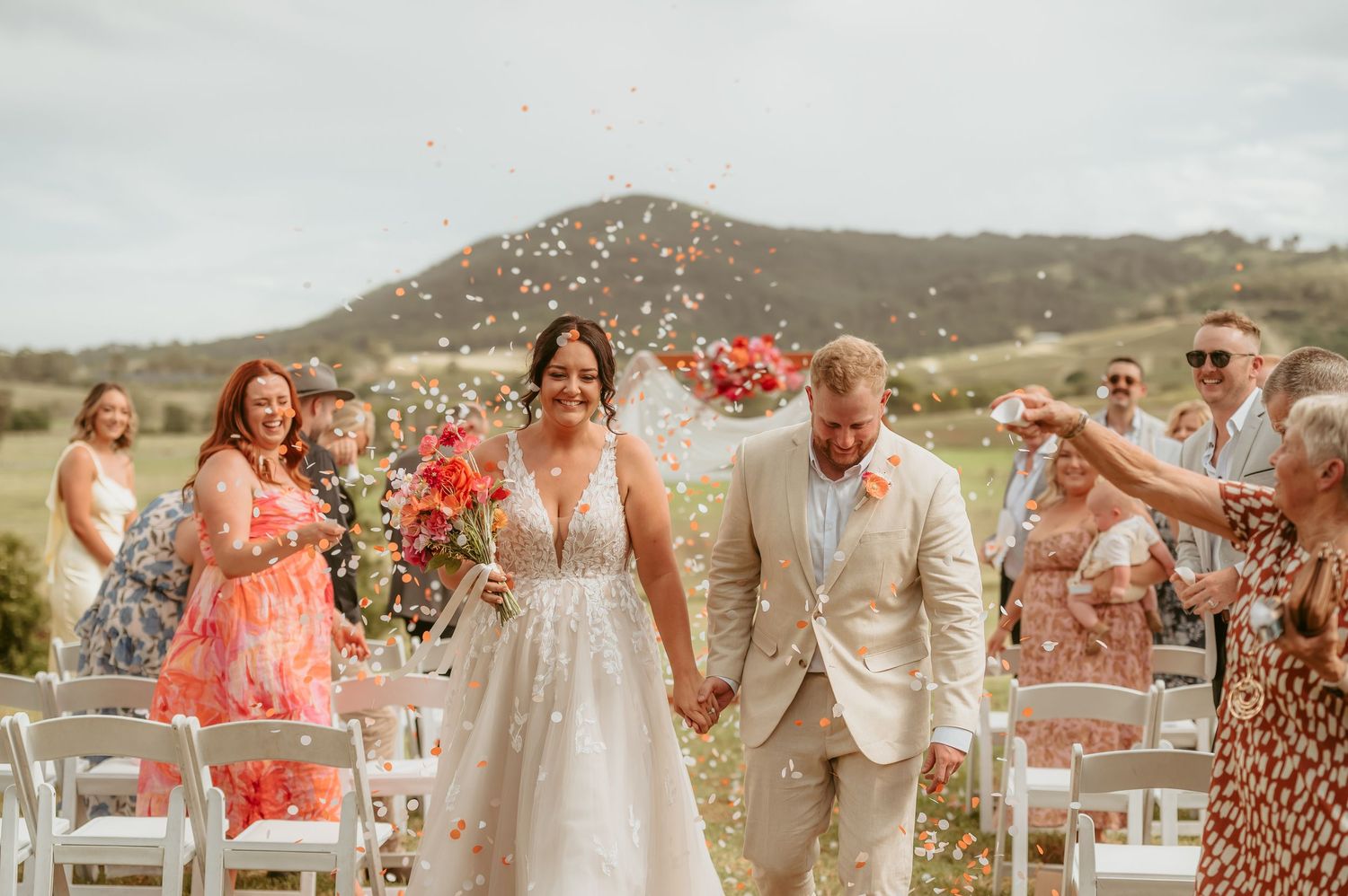 Wedding celebration with guests throwing confetti outdoors against mountain backdrop.