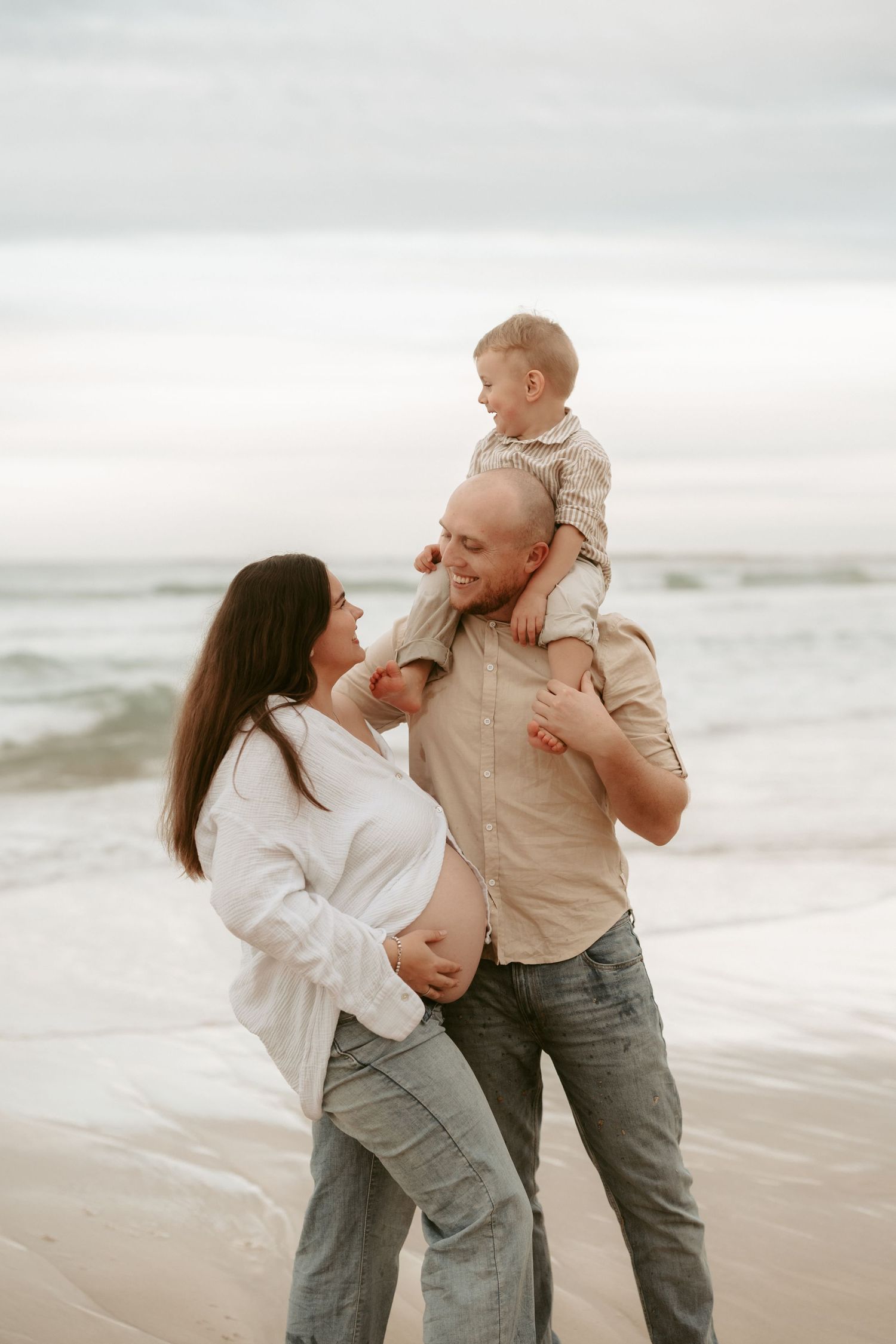 Playful family beach portraits with neutral tones and overcast sky.